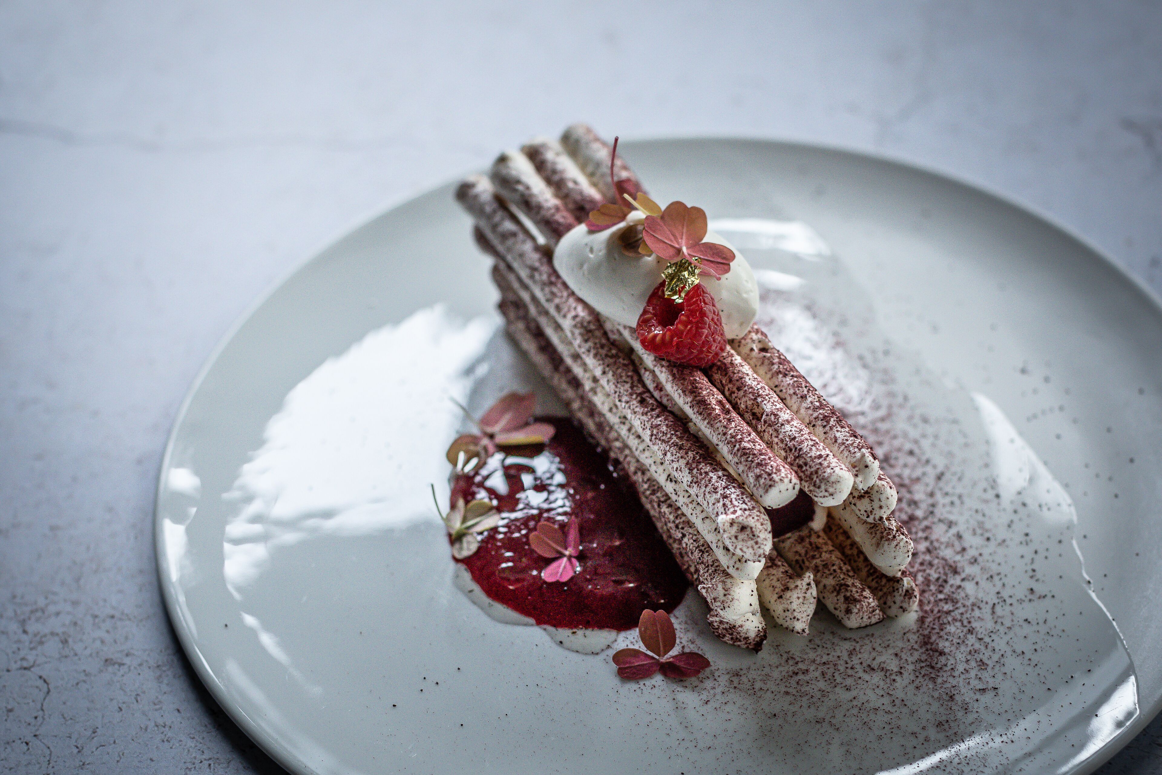 A dessert on a plate with a creamy topping, a berry, and a dusting of cocoa powder.
