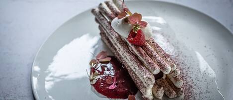 A dessert on a plate with a creamy topping, a berry, and a dusting of cocoa powder.