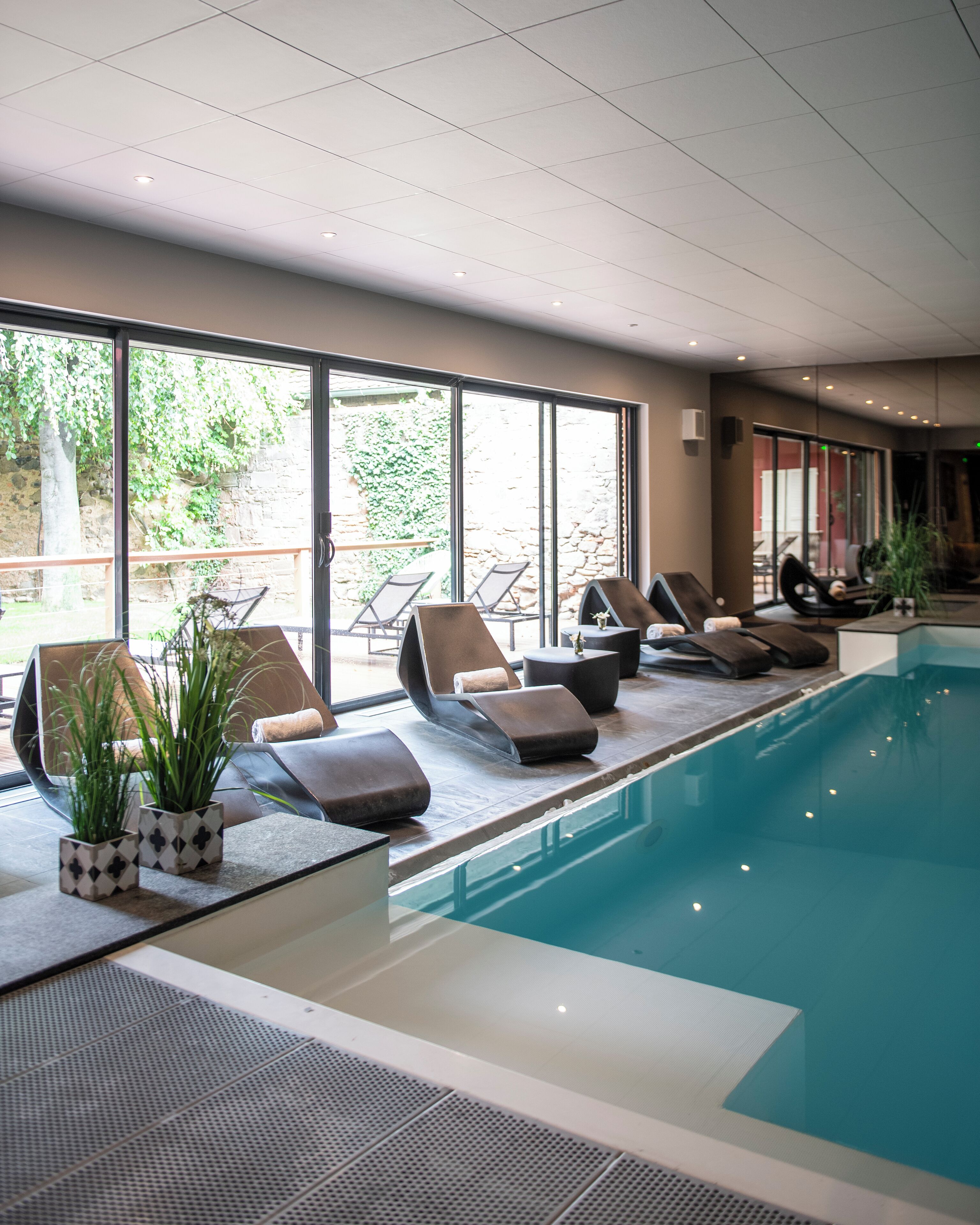 Una piscina interior con sillones de descanso y plantas en macetas.
