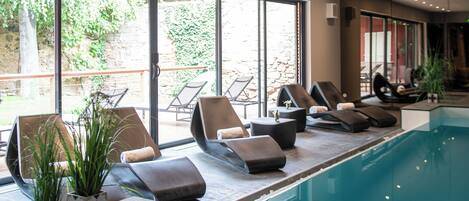 Una piscina interior con sillones de descanso y plantas en macetas.