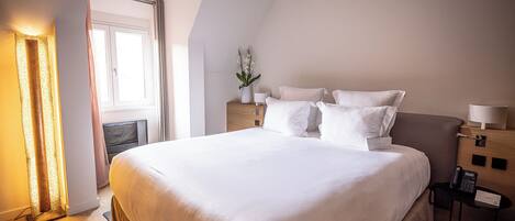 A hotel room with a large bed, bedside tables, a nightstand, a lamp, and a window.