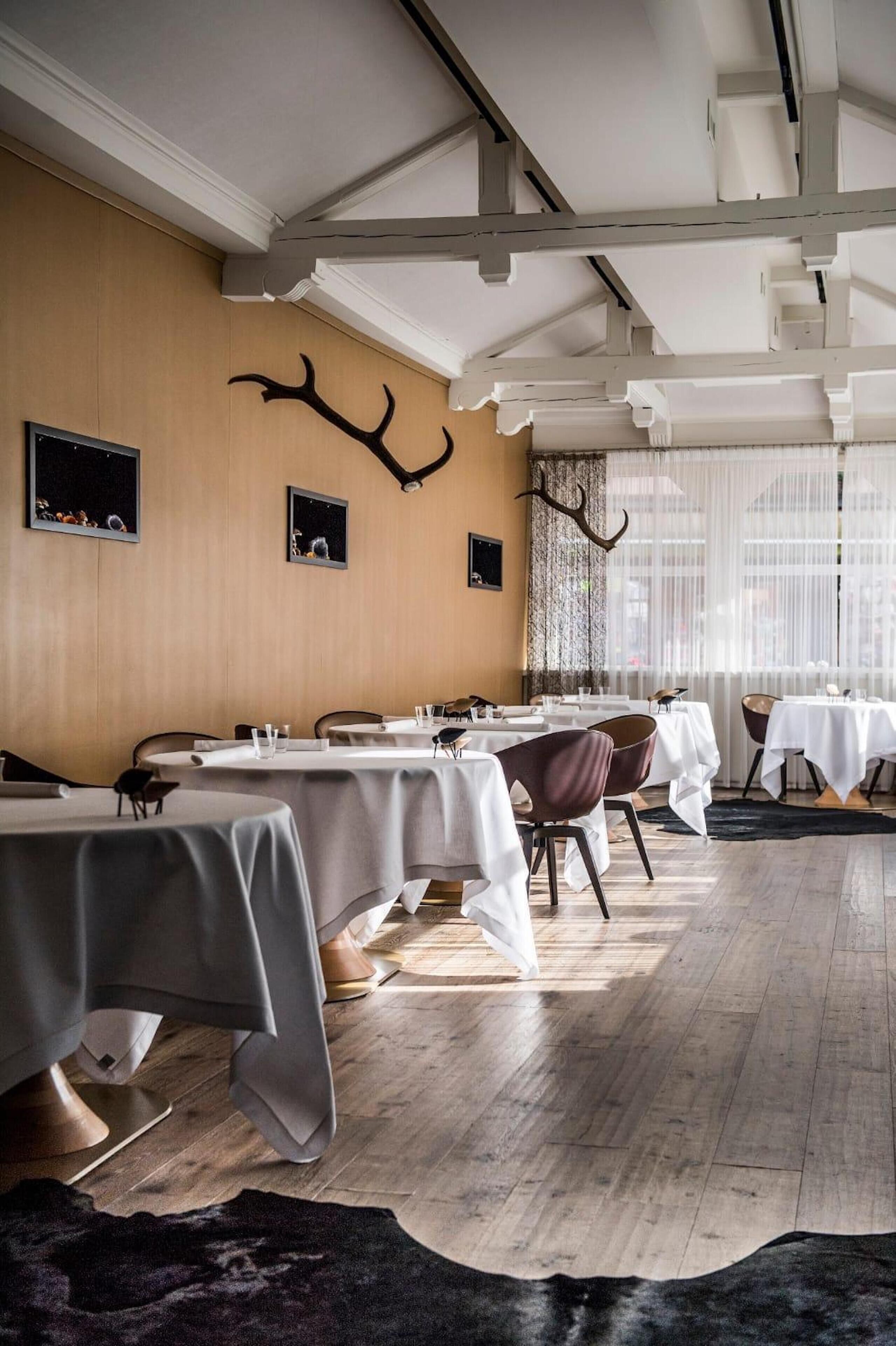 A restaurant with round tables, white tablecloths, and antler decorations on the wall.