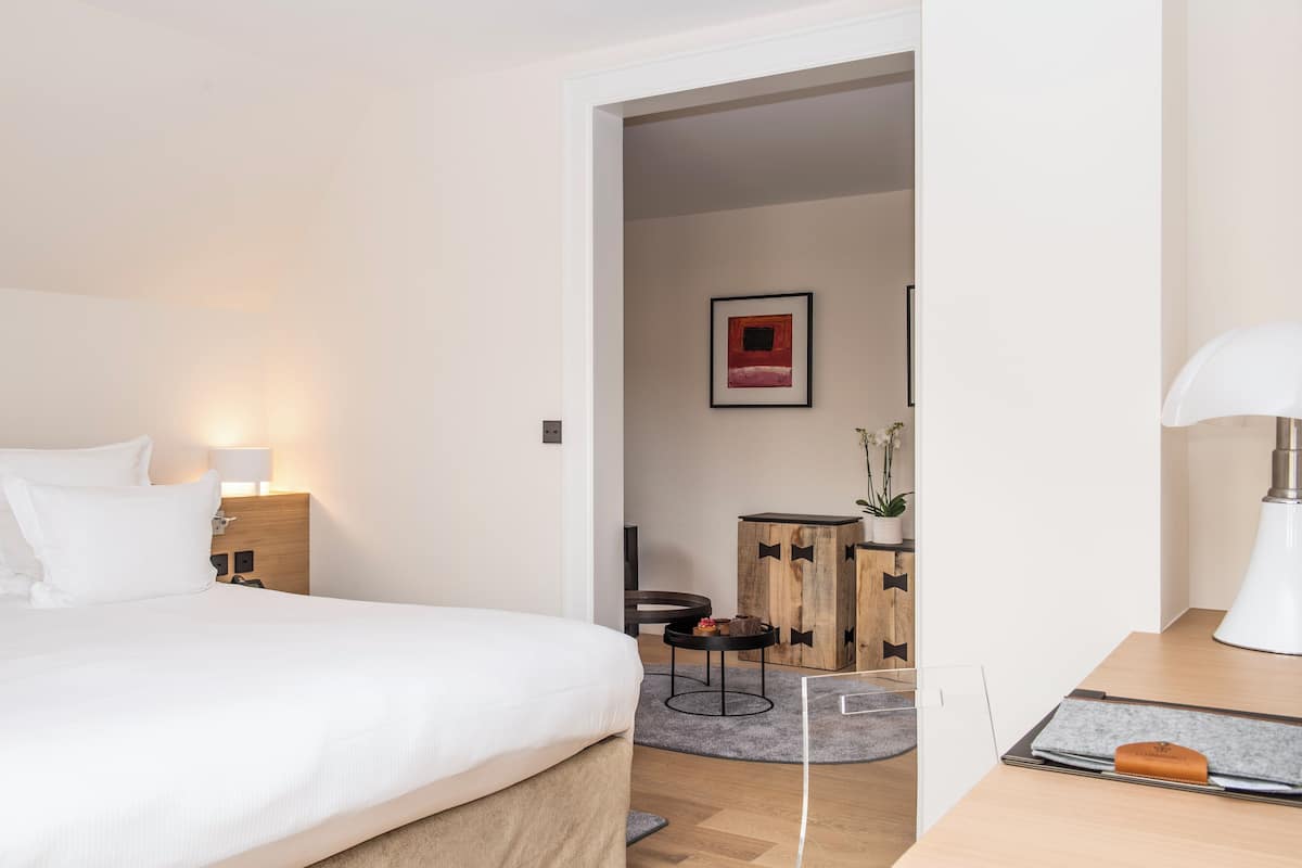 A hotel room with a bed, bedside table, lamp, and a desk with a lamp.