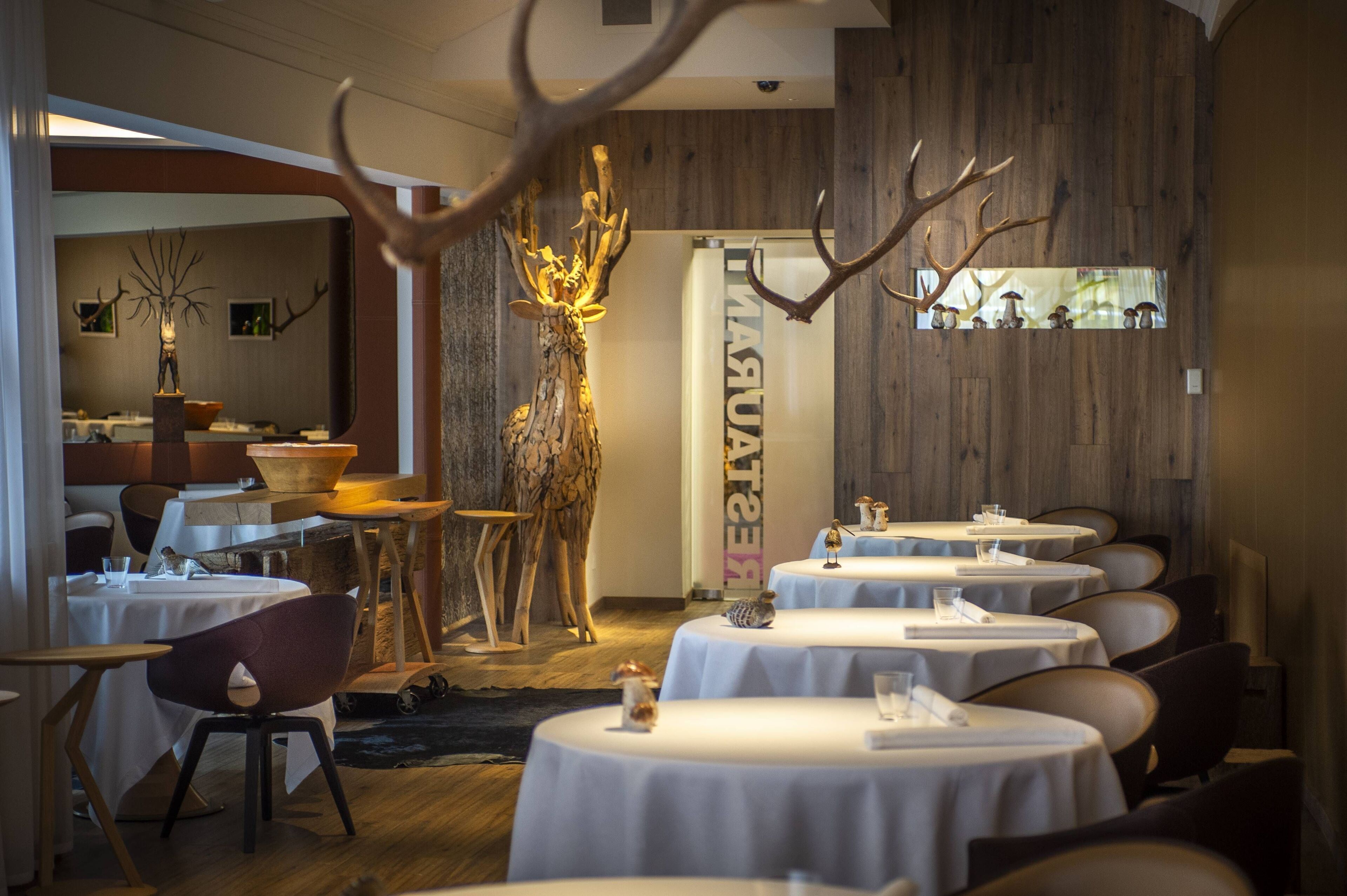 A restaurant with round tables, wooden decor, and antler sculptures.