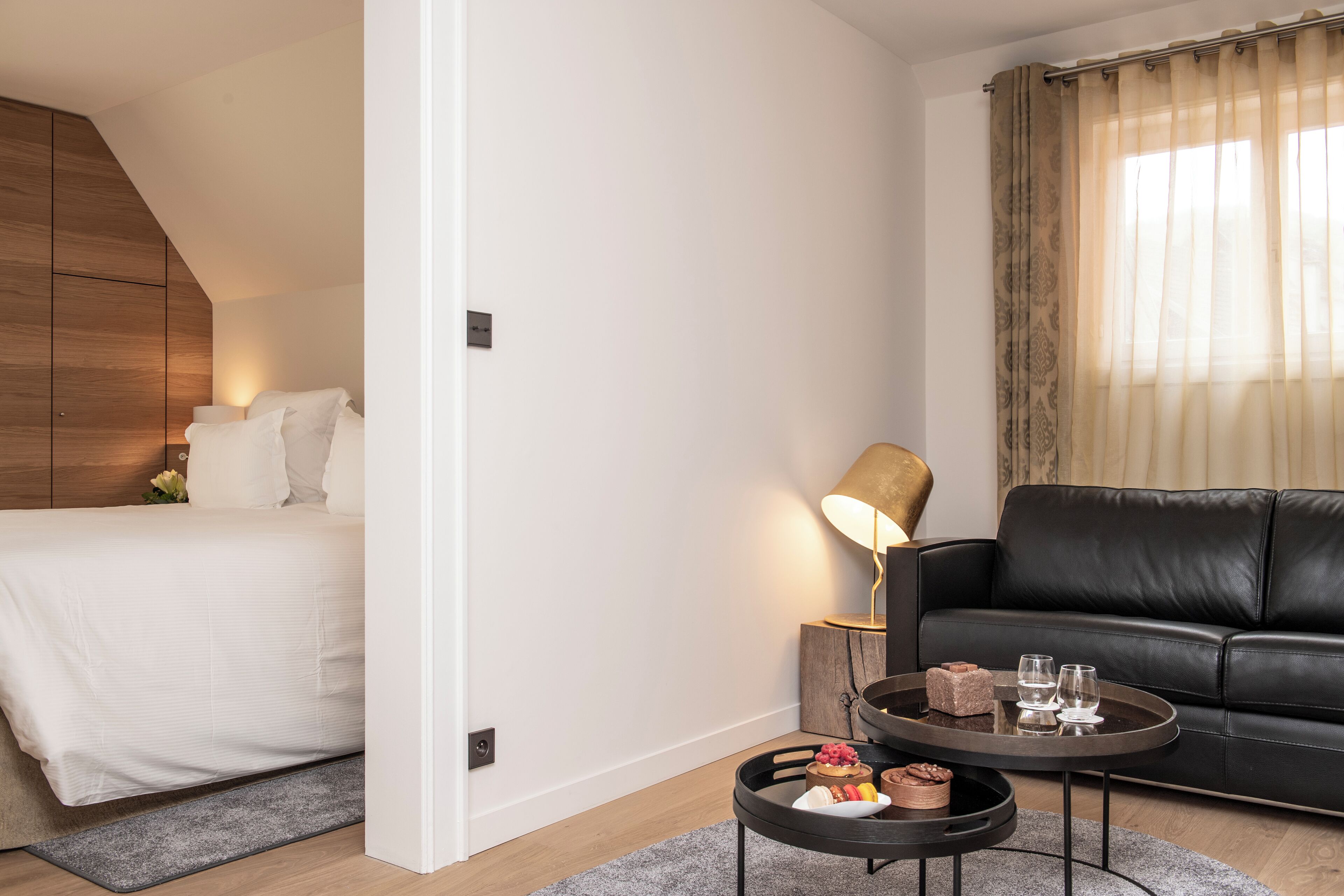 A bedroom with a bed, a bedside table with a lamp, a black leather sofa, and a small round table with a tray.