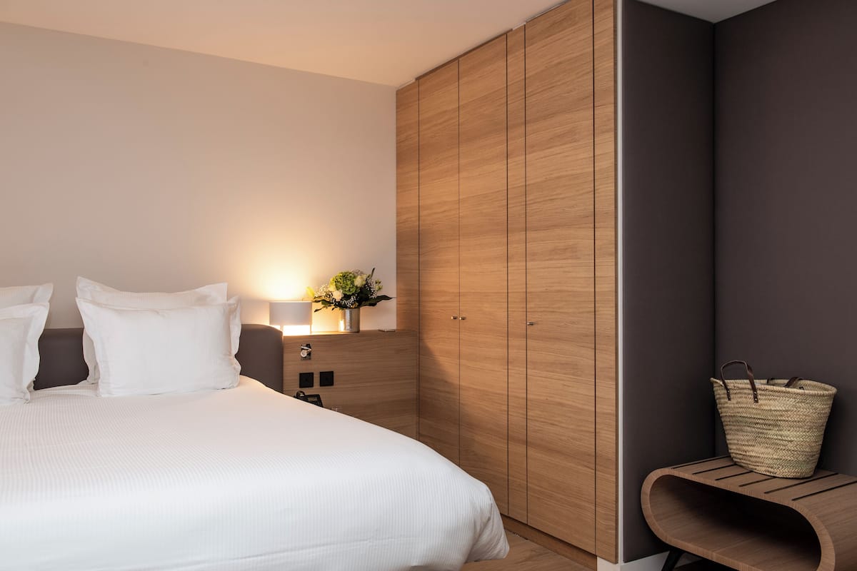A bedroom with a bed, a wooden wardrobe, a bedside table with a lamp, and a woven basket.