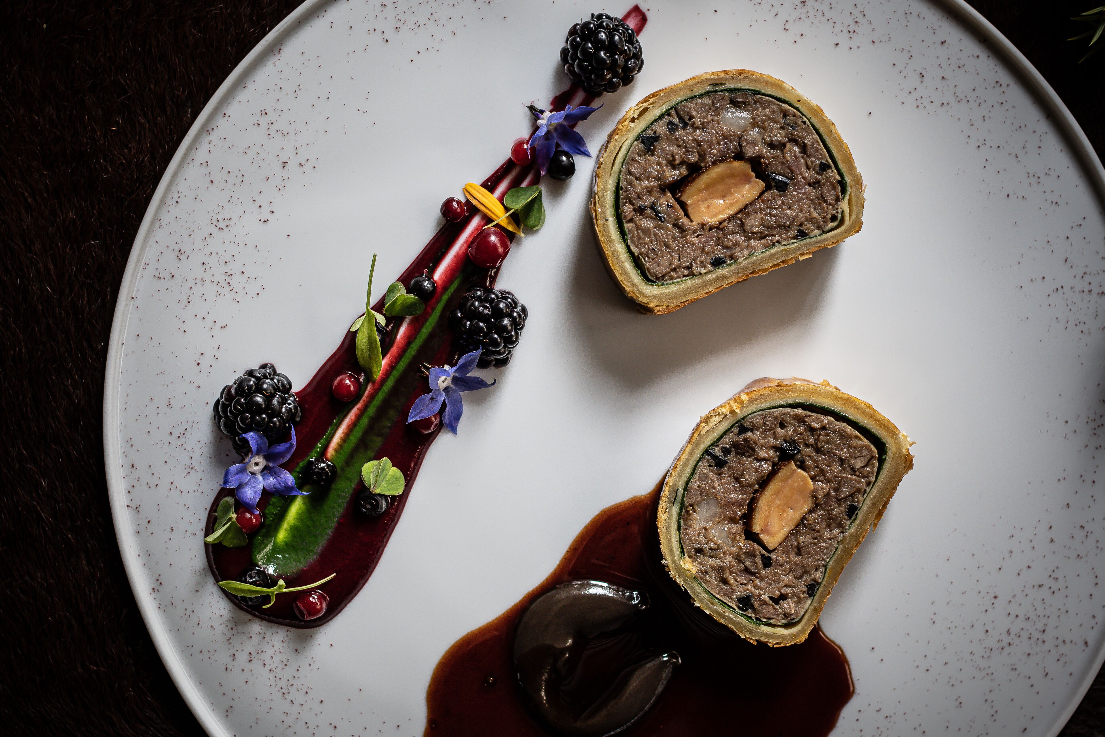 A plate with a rolled meat dish, berries, and a decorative element.
