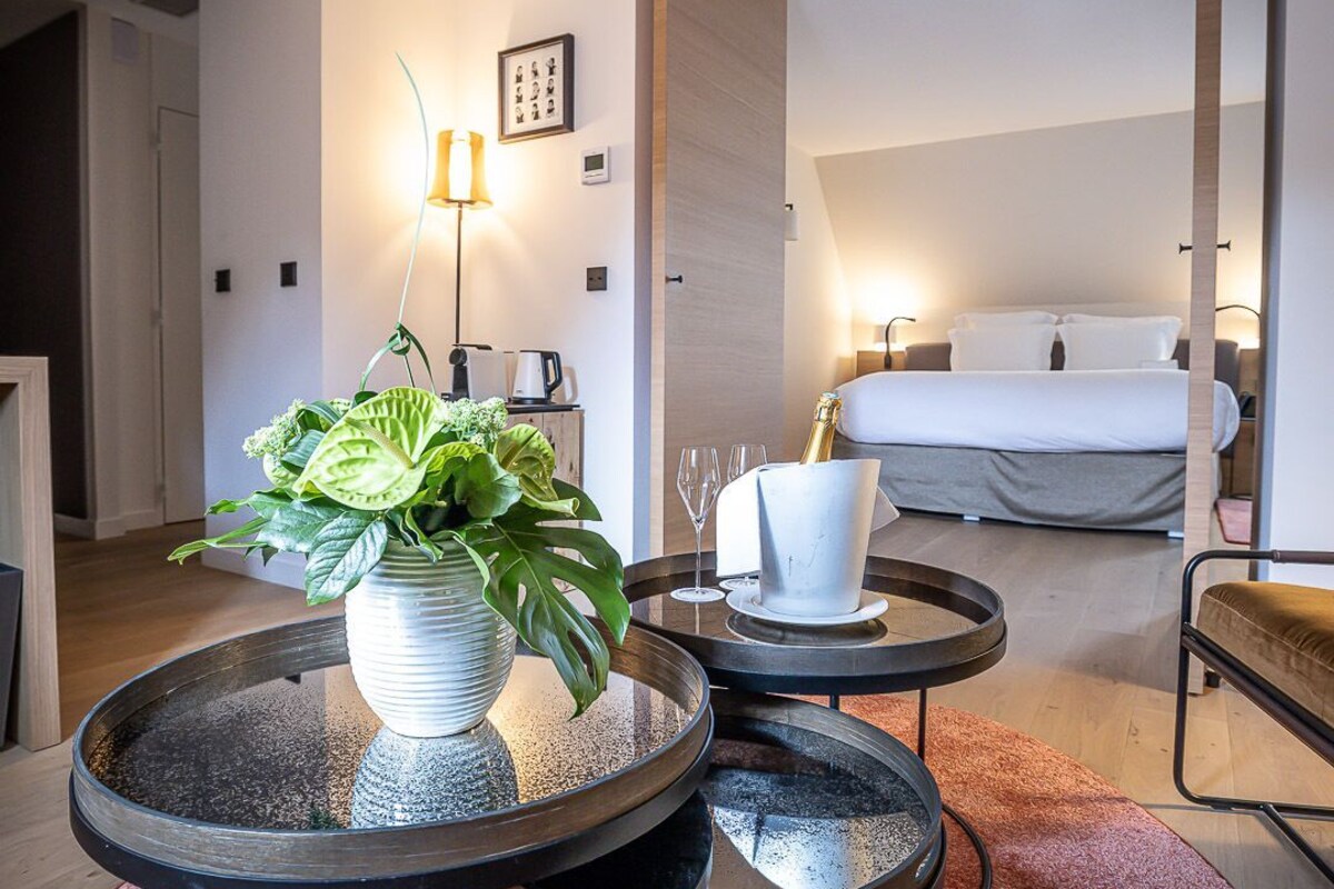 Una habitación de hotel moderna con cama, una mesa de comedor con sillas, una pequeña cocina y una planta en maceta.