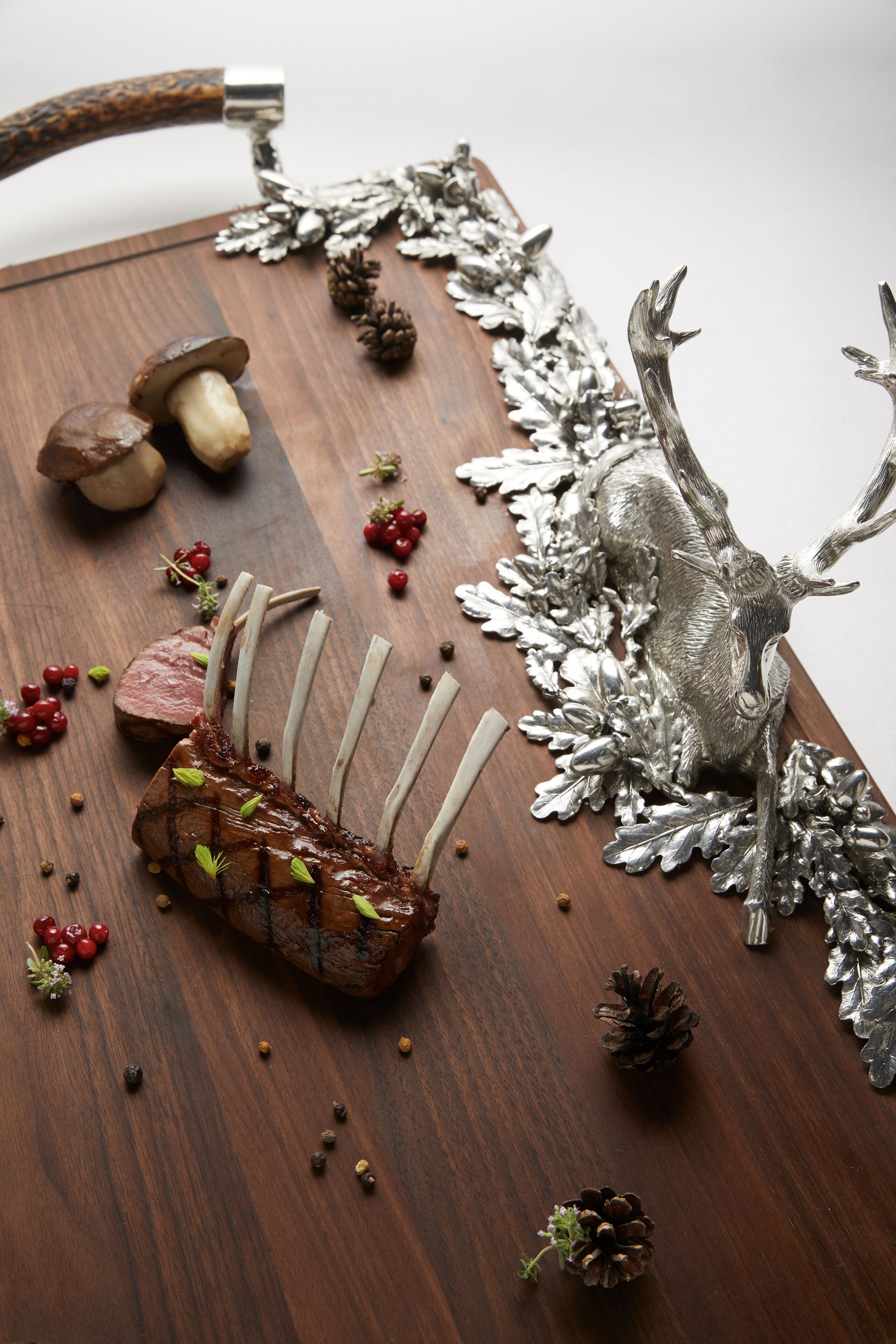 Ein Holztisch mit einem Braten im Mittelpunkt, umgeben von dekorativen Elementen wie Kiefernzapfen und silbernen Hirschgeweihen.