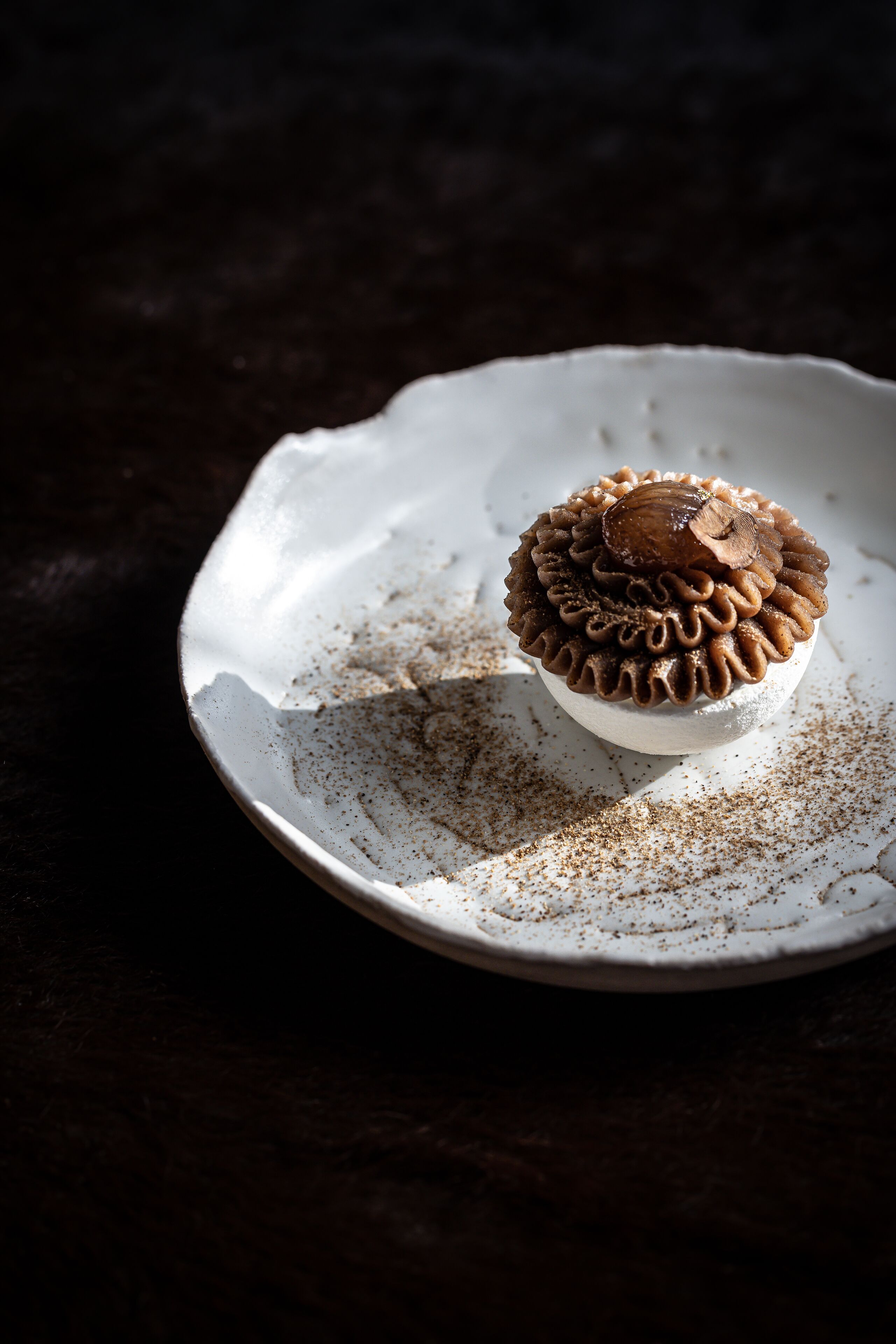 Un postre sobre un plato blanco con borde texturizado, sobre una superficie oscura.