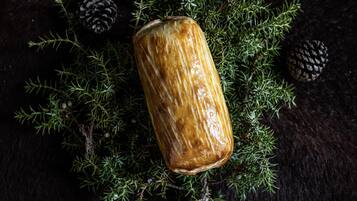 A glass with a wooden texture surrounded by pine branches and cones on a dark surface.