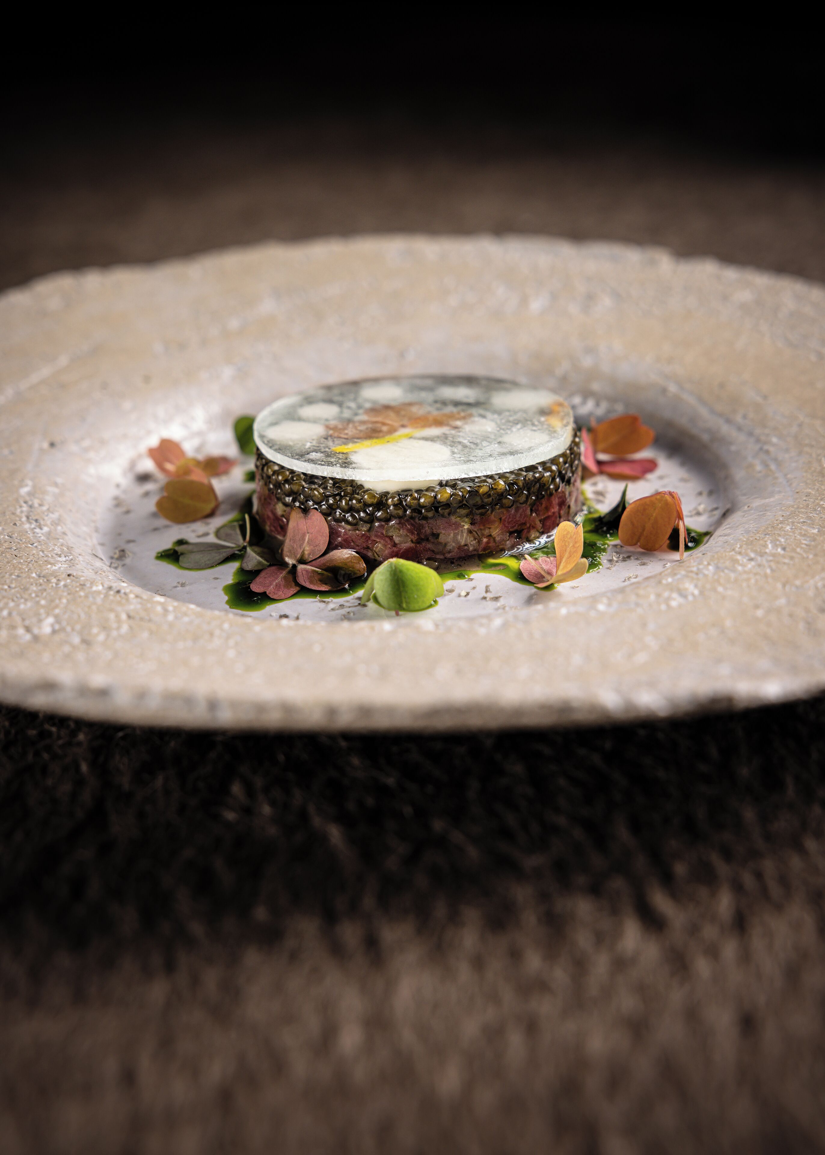 A dessert on a plate with a textured edge, surrounded by scattered leaves and petals.