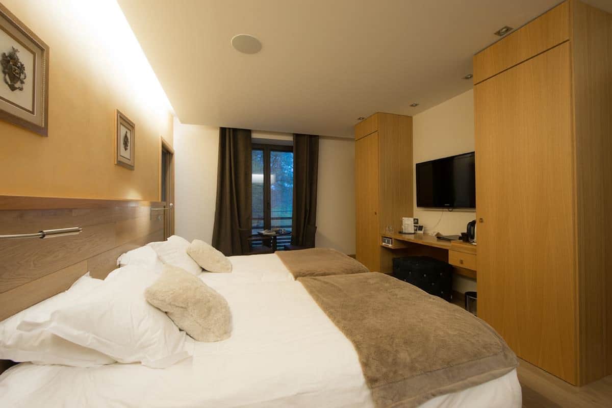 Habitación de hotel con dos camas, un escritorio, un televisor de pantalla plana, un armario y una ventana con cortinas.