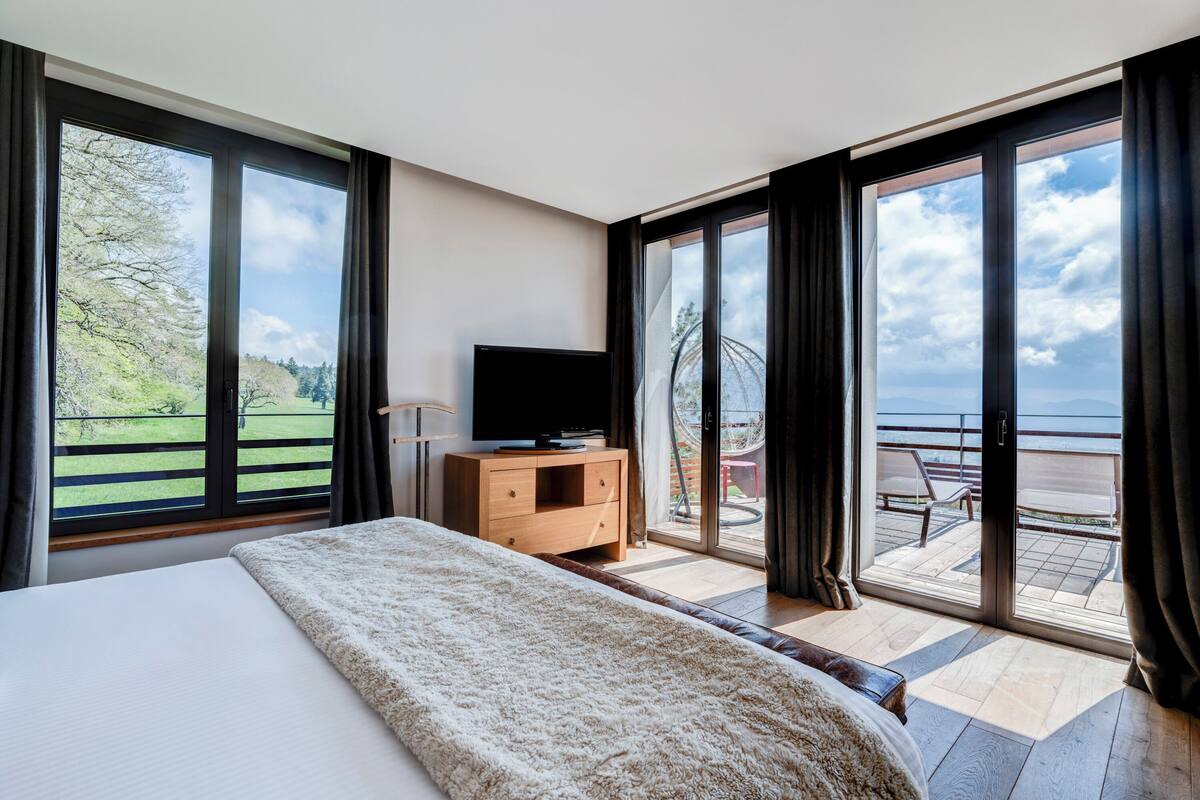 Un dormitorio con una cama grande, un televisor sobre un aparador de madera y un balcón con vistas al mar.