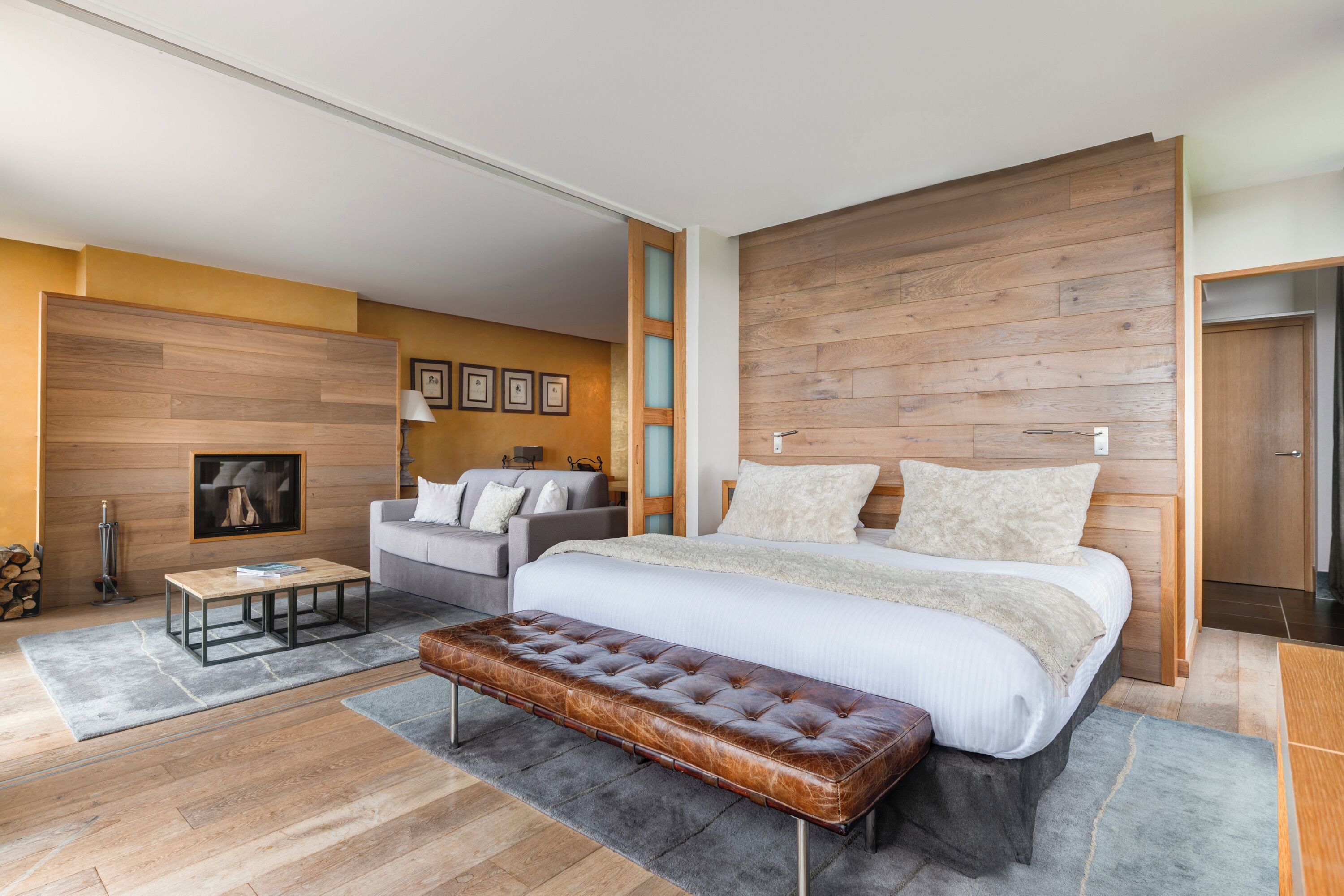 Ein modernes Schlafzimmer mit einem großen Bett, einem hölzernen Kopfteil, einem grauen Sofa, einem Couchtisch und einer Lederbank.