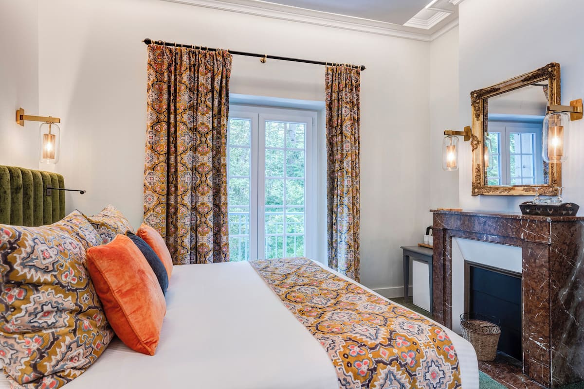 Un dormitorio con una cama grande, cortinas estampadas, chimenea y un espejo.