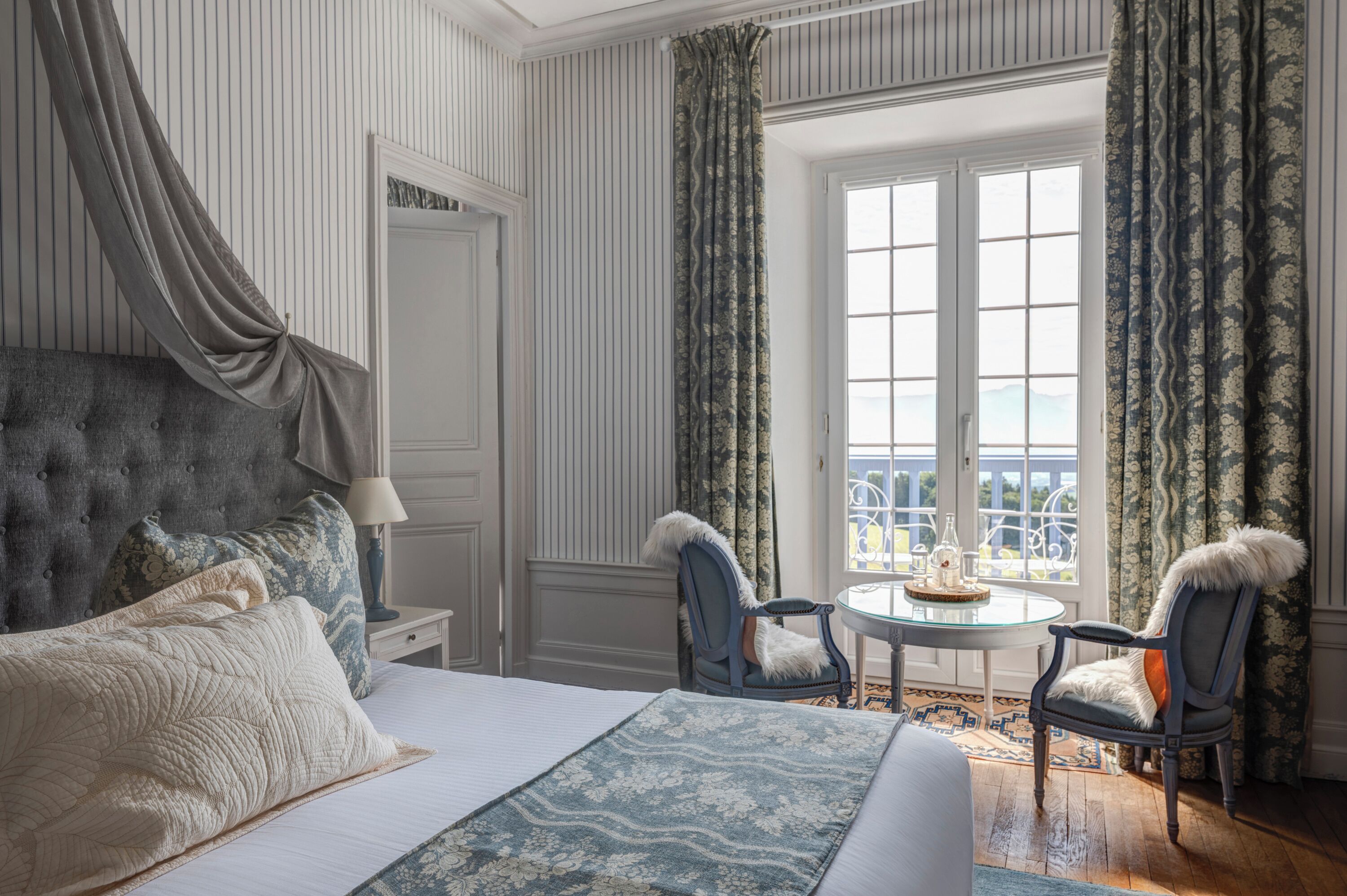 Ein Schlafzimmer mit einem großen Bett, zwei Stühlen, einem kleinen Tisch und einem Fenster mit Vorhängen.
