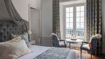 Ein Schlafzimmer mit einem großen Bett, zwei Stühlen, einem kleinen Tisch und einem Fenster mit Vorhängen.