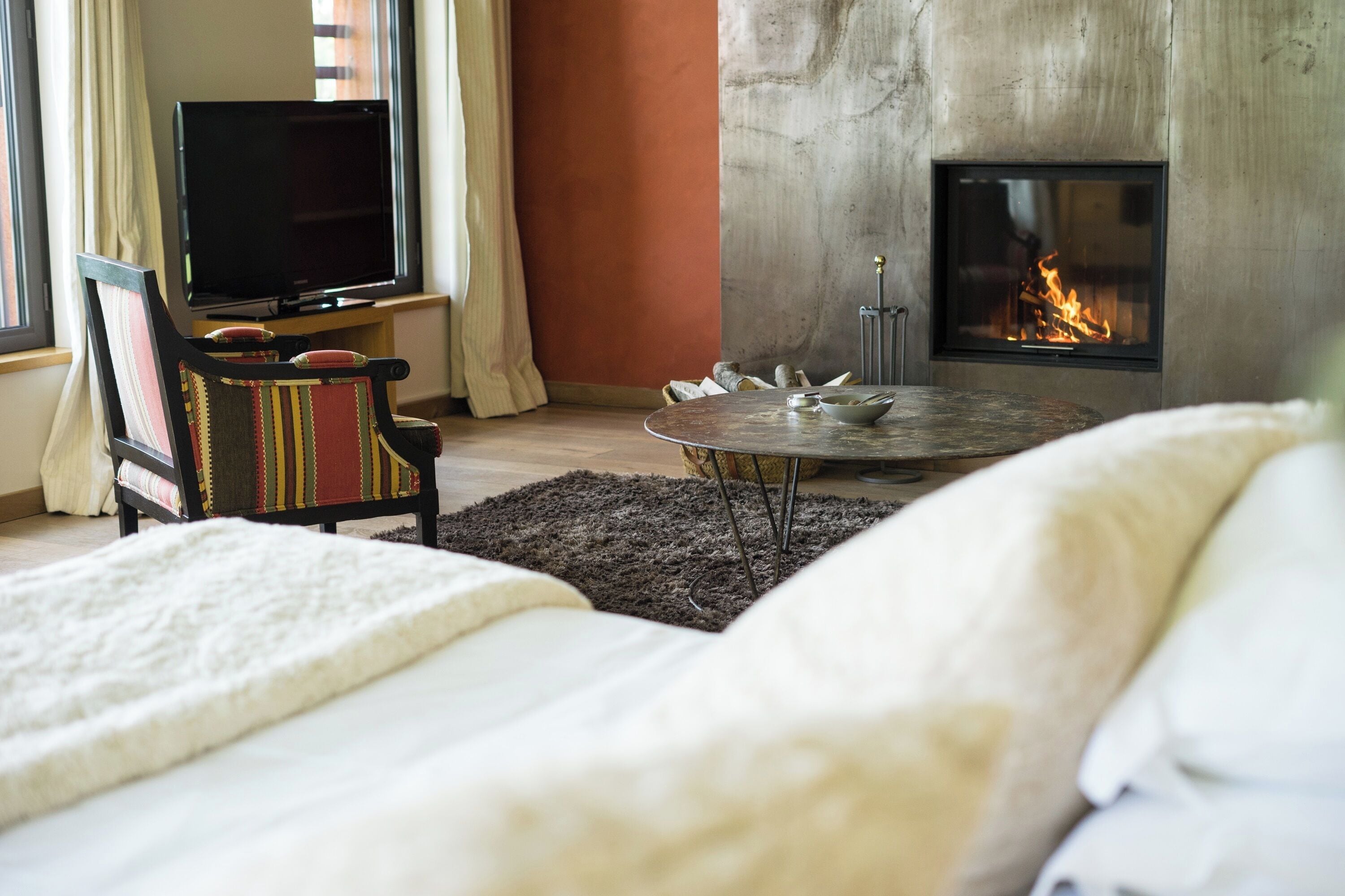 A cozy room with a bed, a round table, a television, and a fireplace.