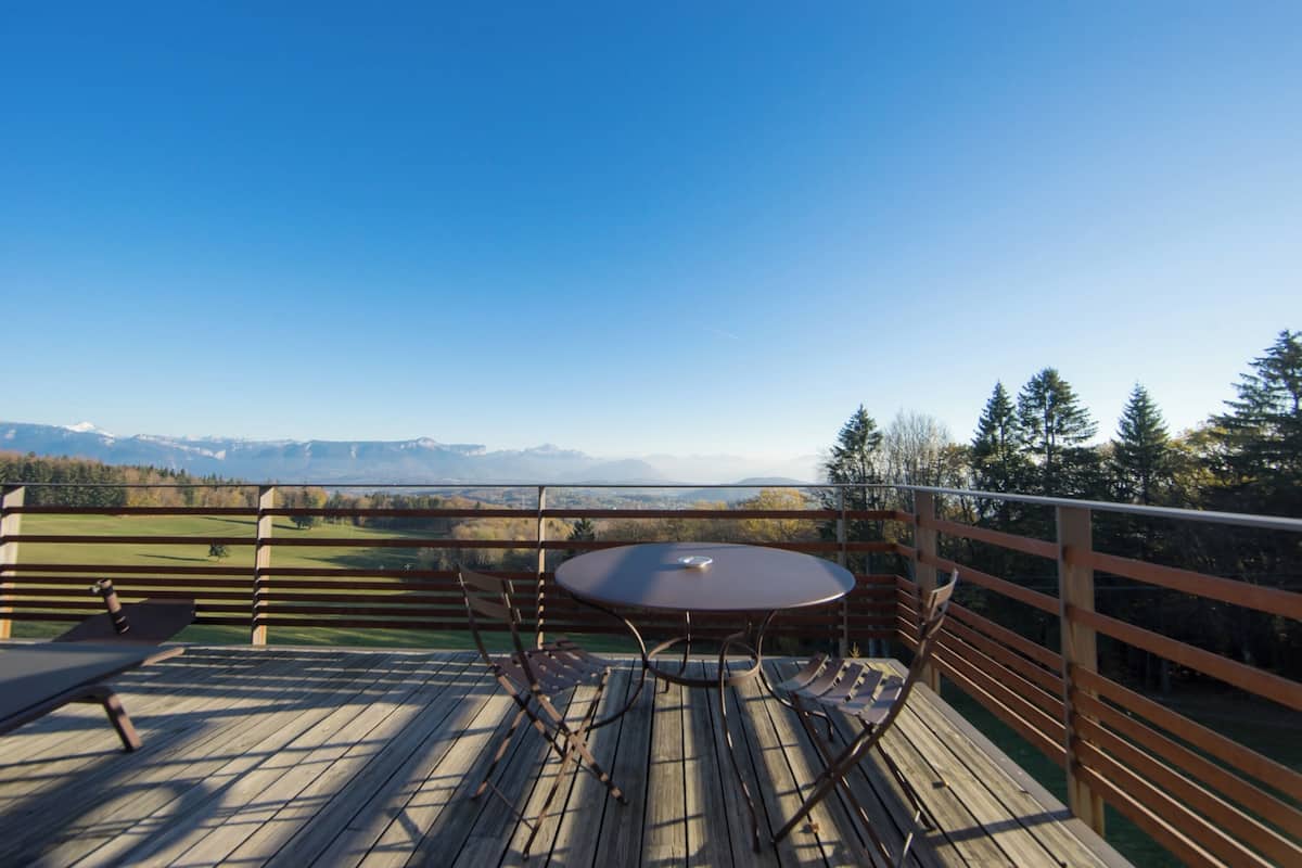Una terraza de madera con una mesa redonda y sillas, con vistas a un paisaje montañoso.