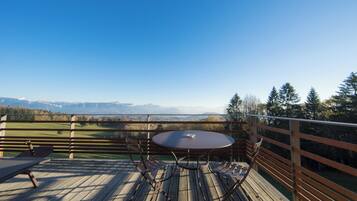 Une terrasse en bois avec une table ronde et des chaises, offrant une vue sur un paysage montagneux.