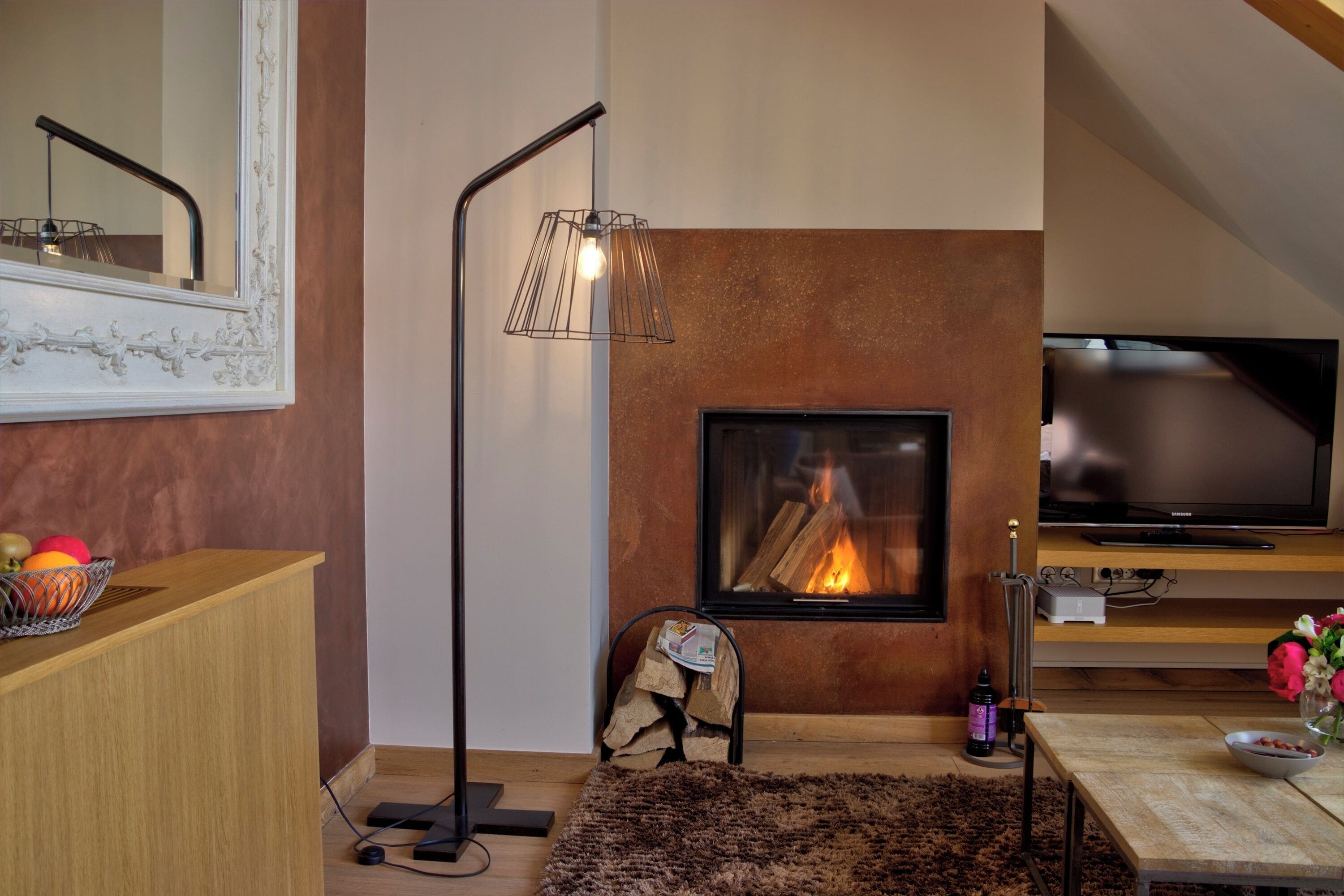 Ein gemütliches Wohnzimmer mit Kamin, Fernseher und einer modernen Stehlampe.