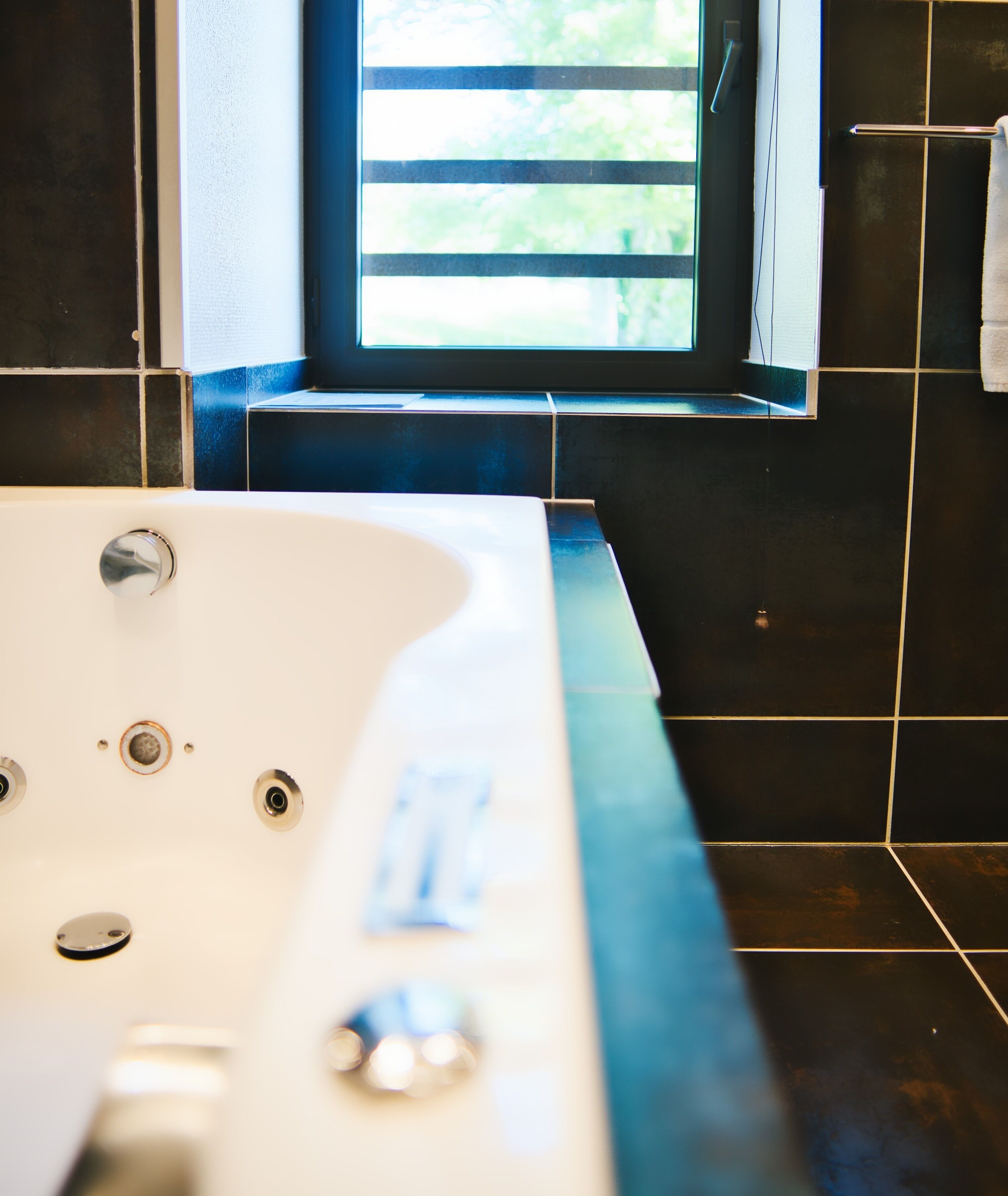 A bathroom with a bathtub, a window, and black tiled walls.