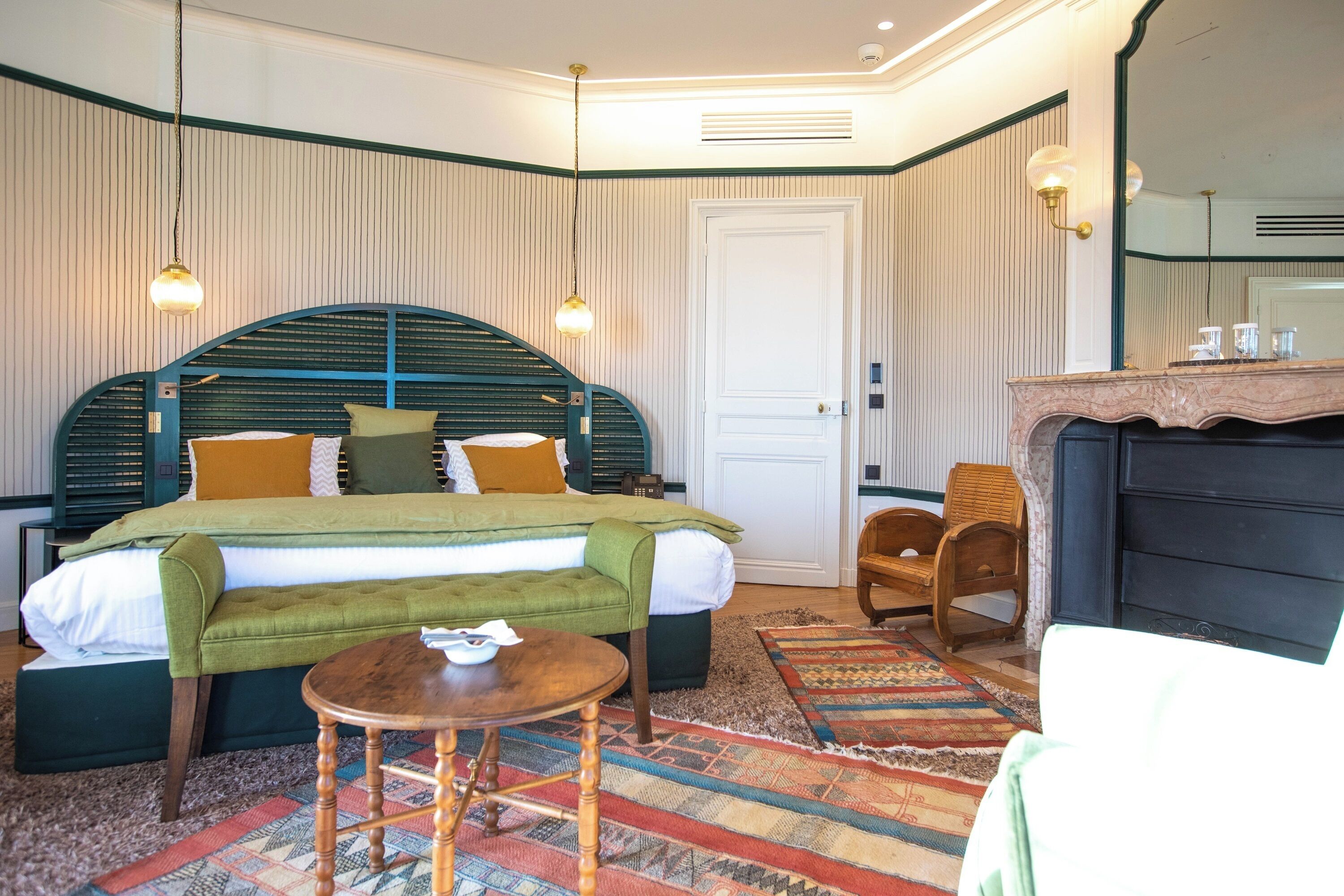 Une chambre à coucher avec un grand lit, une chaise en bois, une petite table et une cheminée.