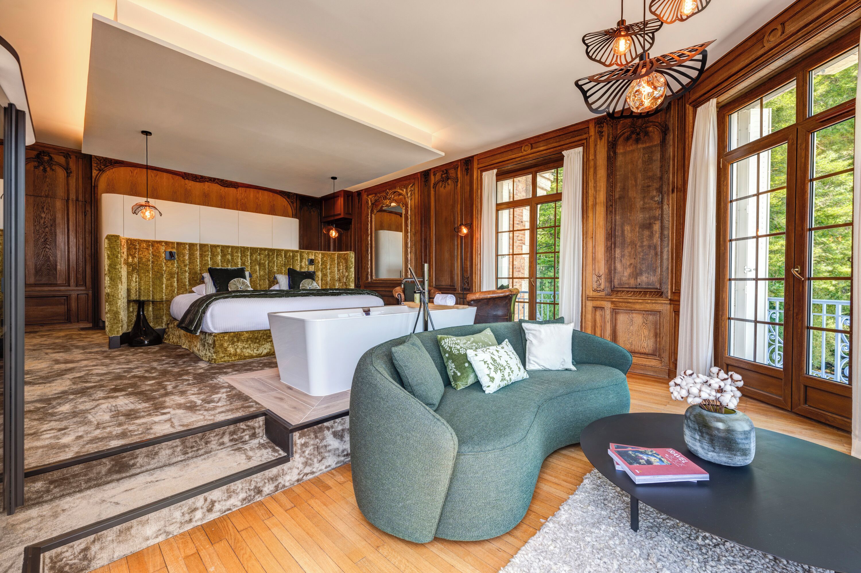 A spacious bedroom with a large bed, a sitting area with a sofa, and a view of the outdoors through large windows.