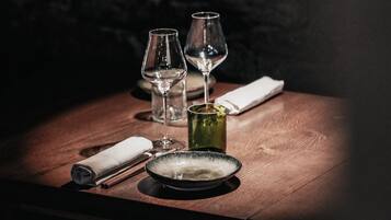A table with a glass, a green bottle, a rolled napkin, and a plate.