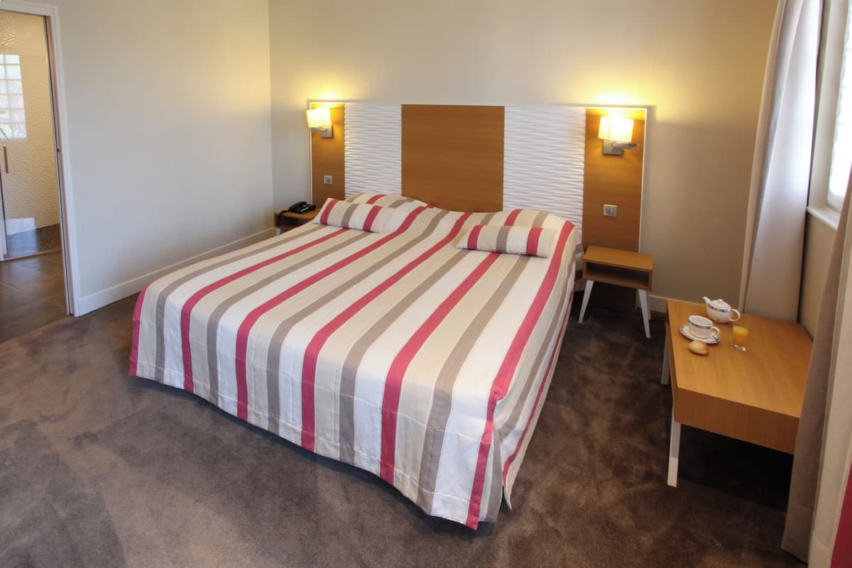 A hotel room with a large bed, bedside lamps, a nightstand, and a small table with a phone and a cup.