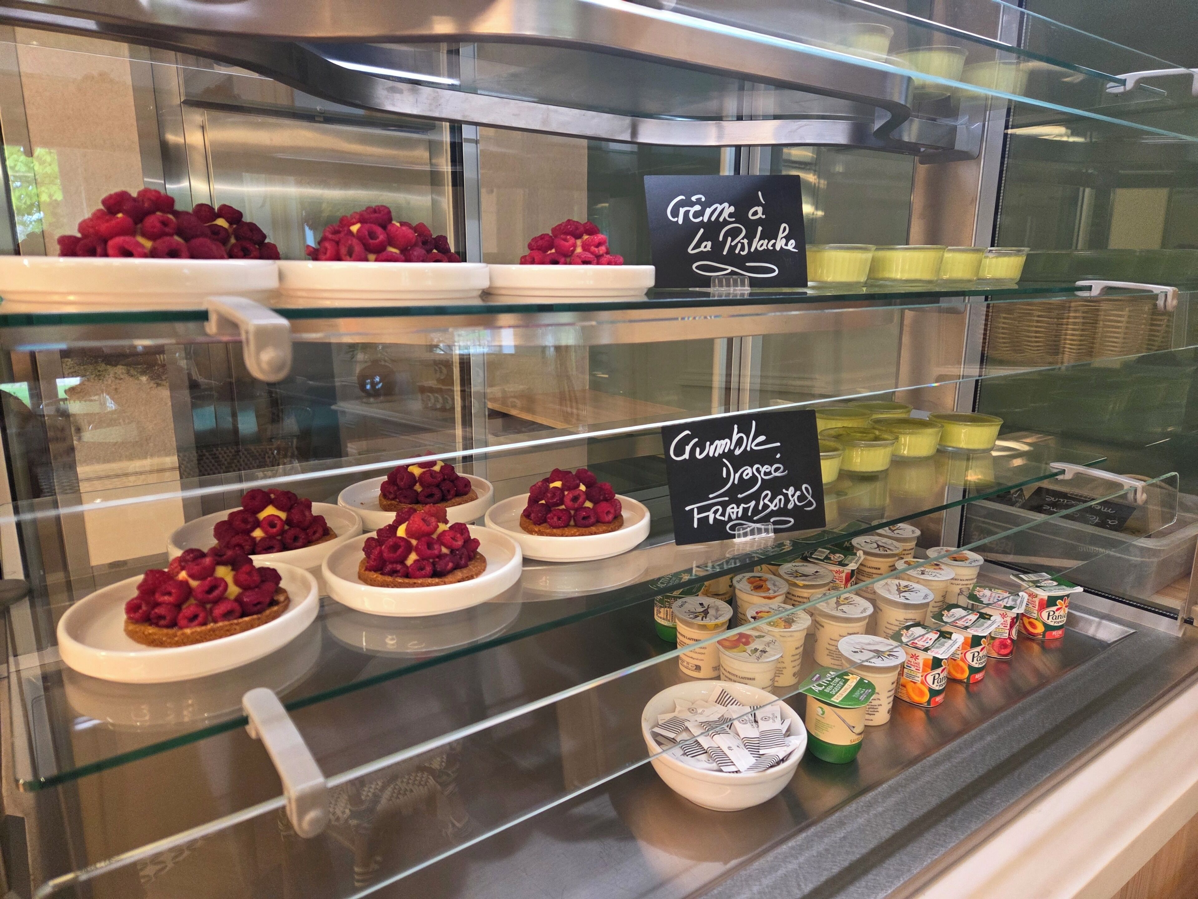A display case with desserts, including a sign for 'Crème à La Pistache' and 'Grumble Yogee Fruit Bowls.'