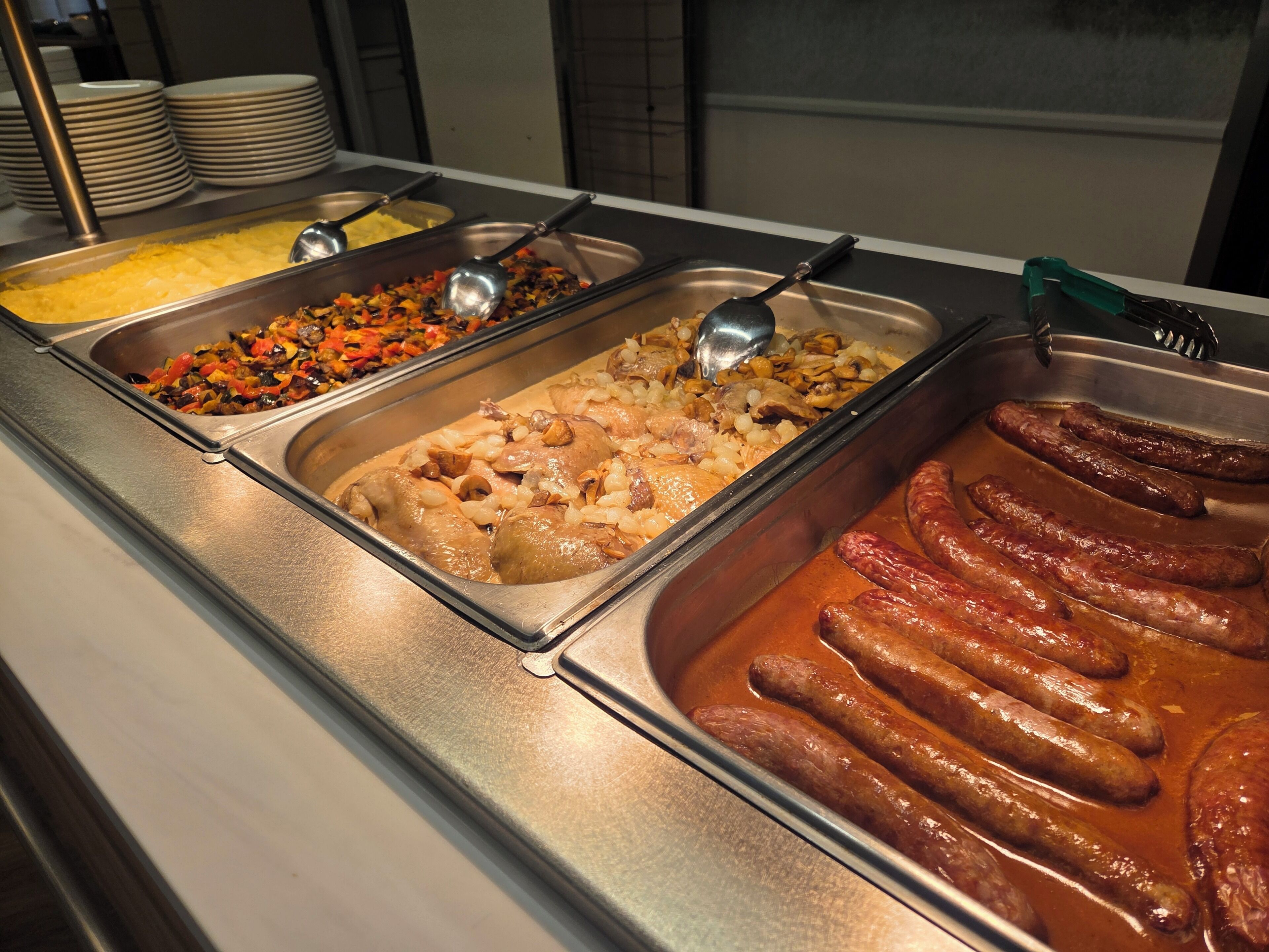 Un bufé con diversos platos, incluyendo salchichas, verduras y un pastel de carne.