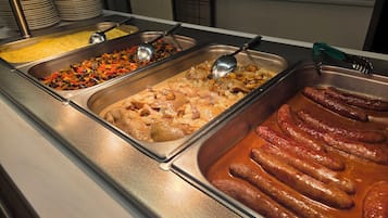 Un bufé con diversos platos, incluyendo salchichas, verduras y un pastel de carne.