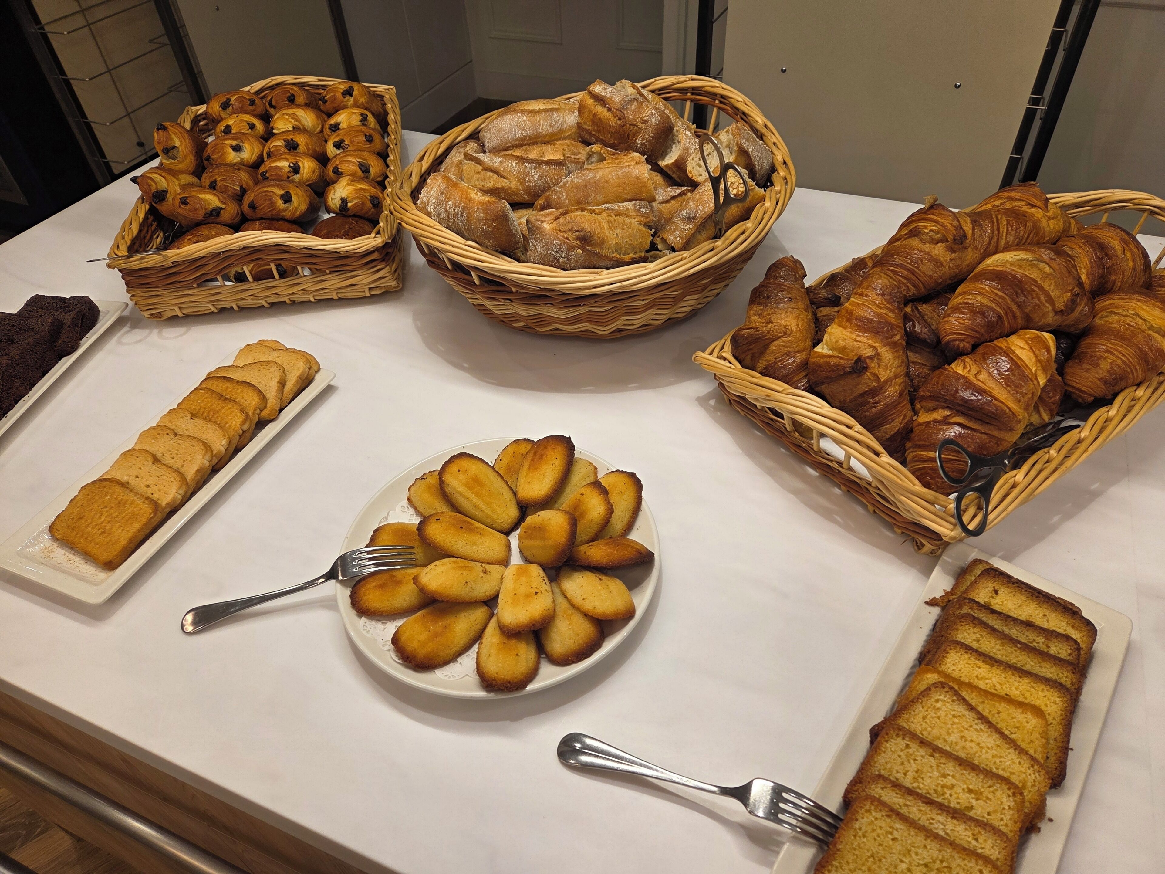 A buffet table with various baked goods including croissants, bread, and pastries.