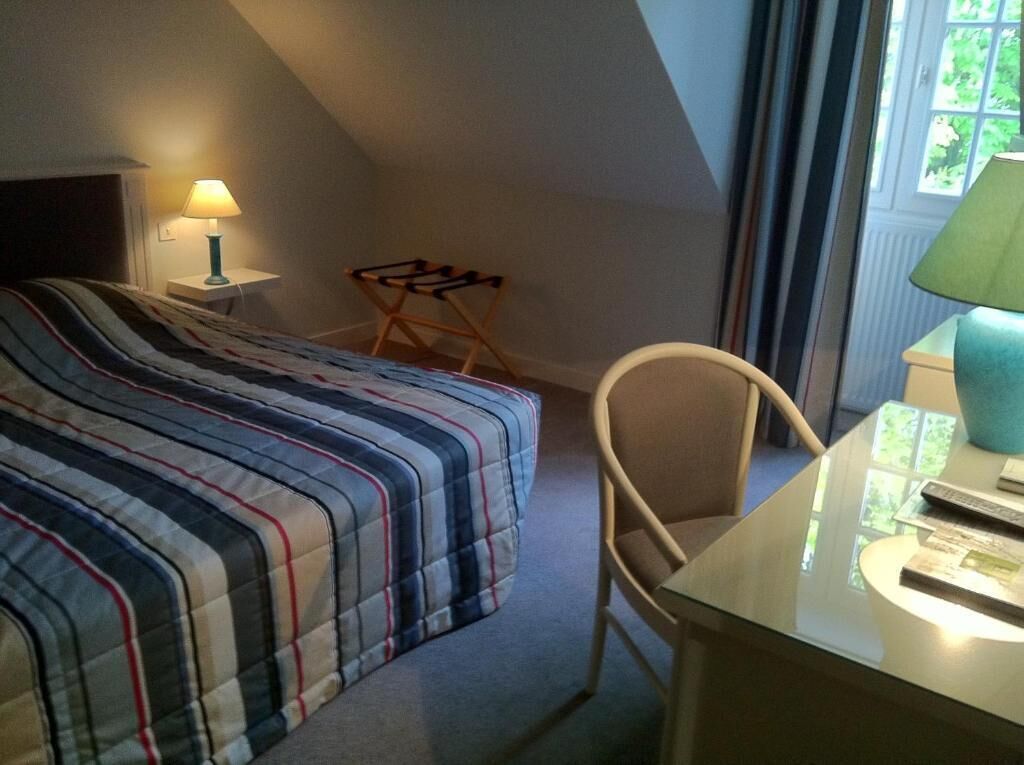 Un dormitorio con cama, escritorio, silla, lámpara y ventana.