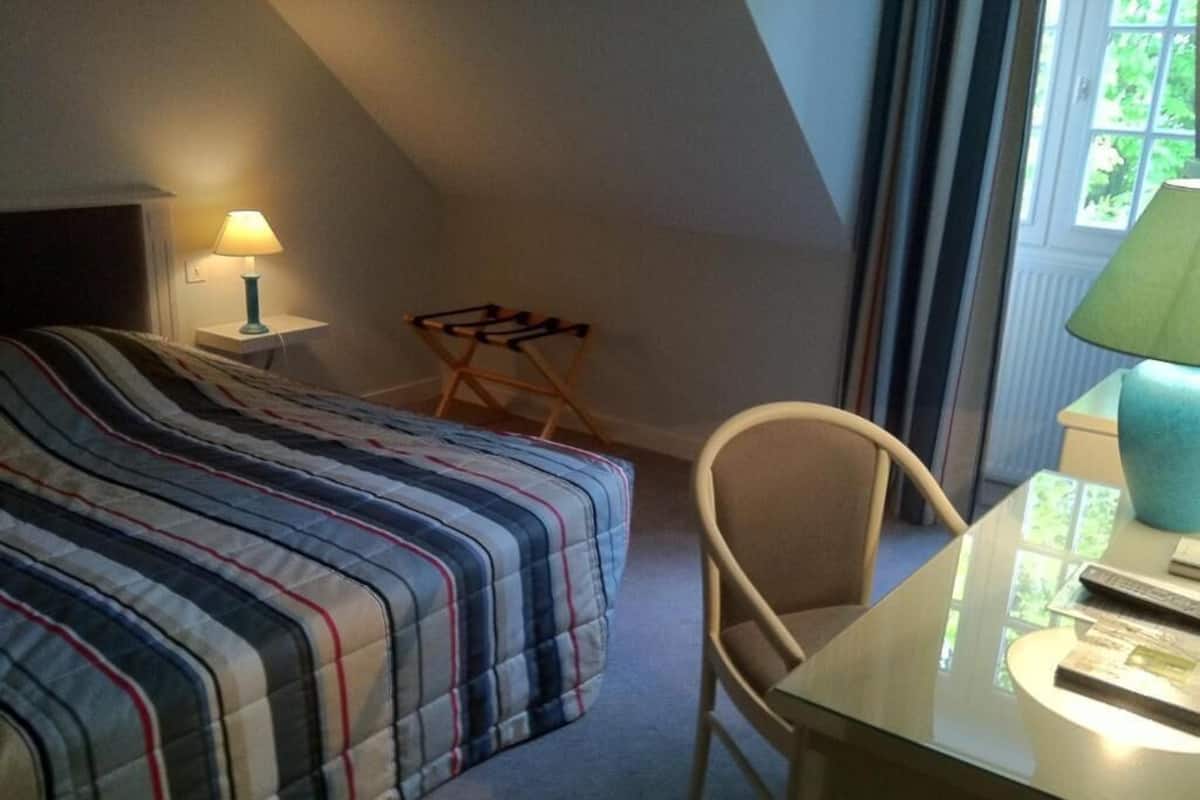 A bedroom with a bed, a desk, a chair, a lamp, and a window.