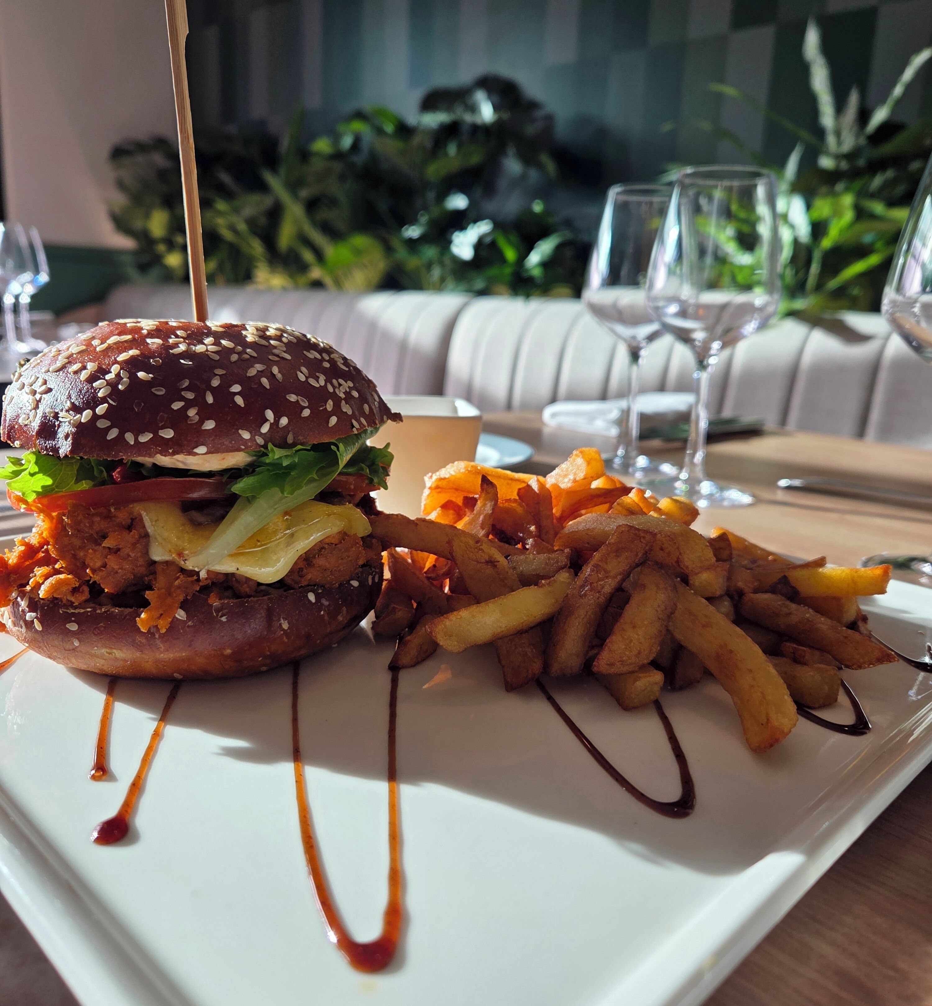 Un plato con una hamburguesa y papas fritas, un vaso de agua y un vaso de vino sobre una mesa.