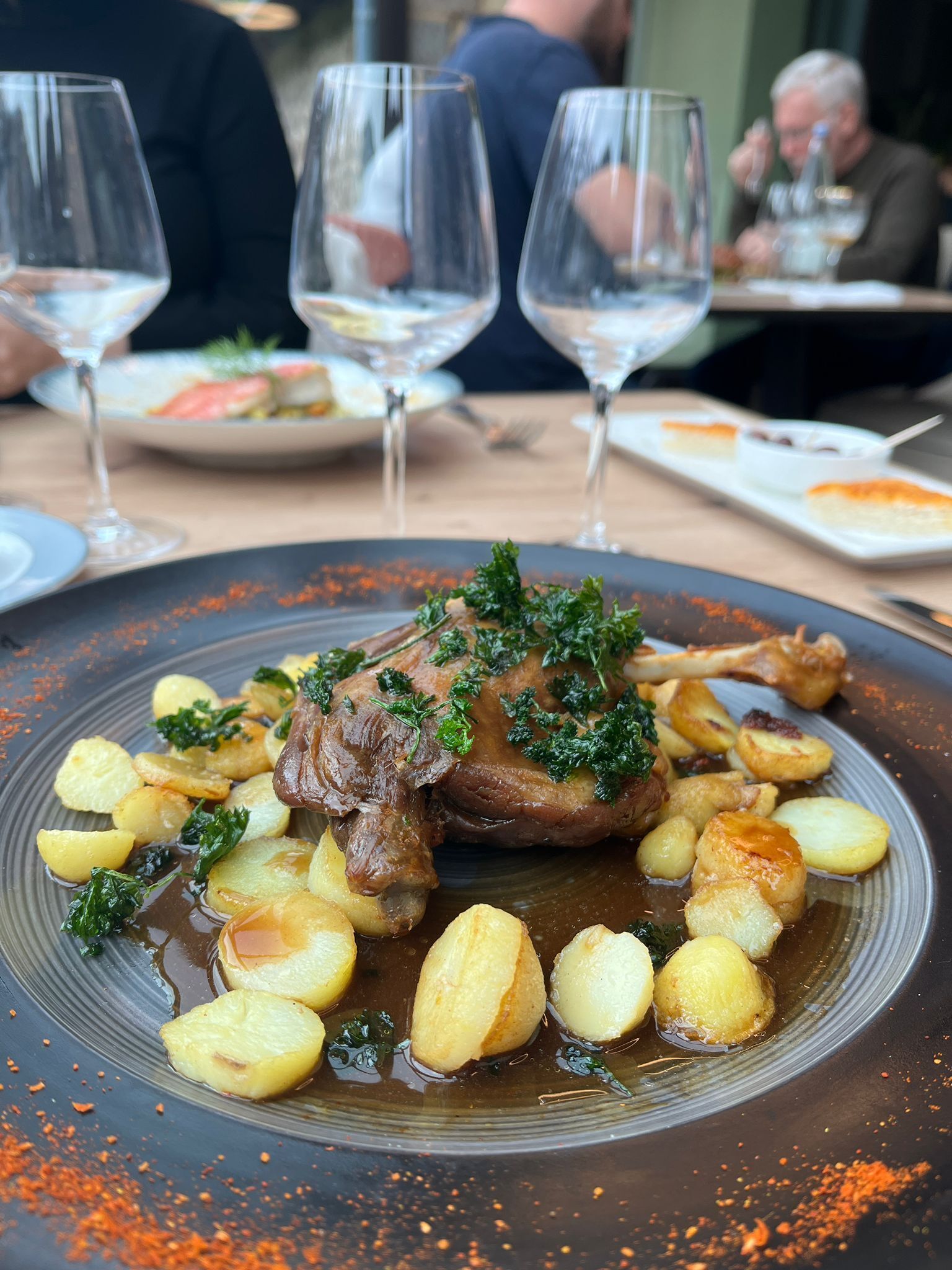 Una mesa de comedor con un plato de comida, copas de vino y una persona al fondo.