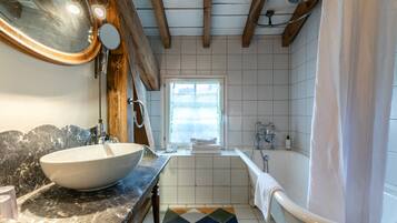 Un baño con un lavamanos de pedestal grande, una bañera, una ventana y suelo de baldosas.