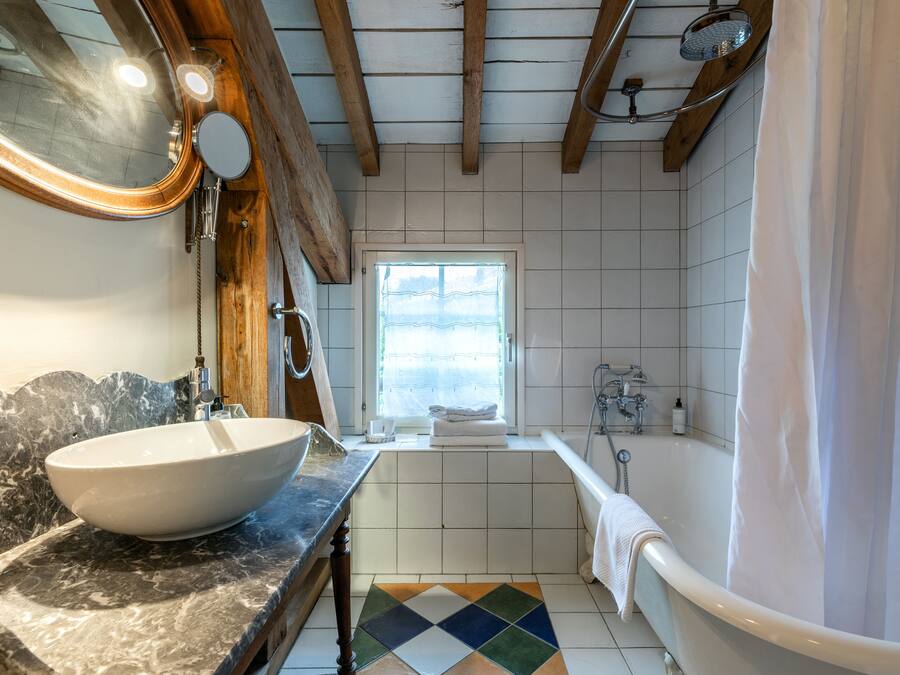 Un baño con un lavamanos de pedestal grande, una bañera, una ventana y suelo de baldosas.