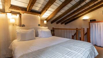 A bedroom with a large bed, wooden beams, and two wall-mounted lamps.