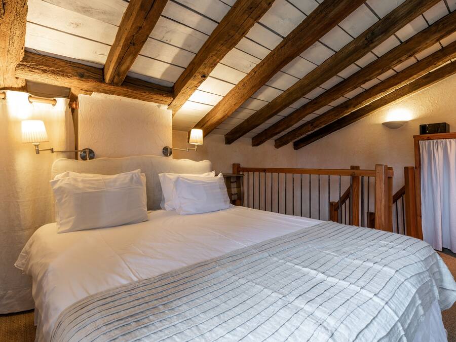 A bedroom with a large bed, wooden beams, and two wall-mounted lamps.