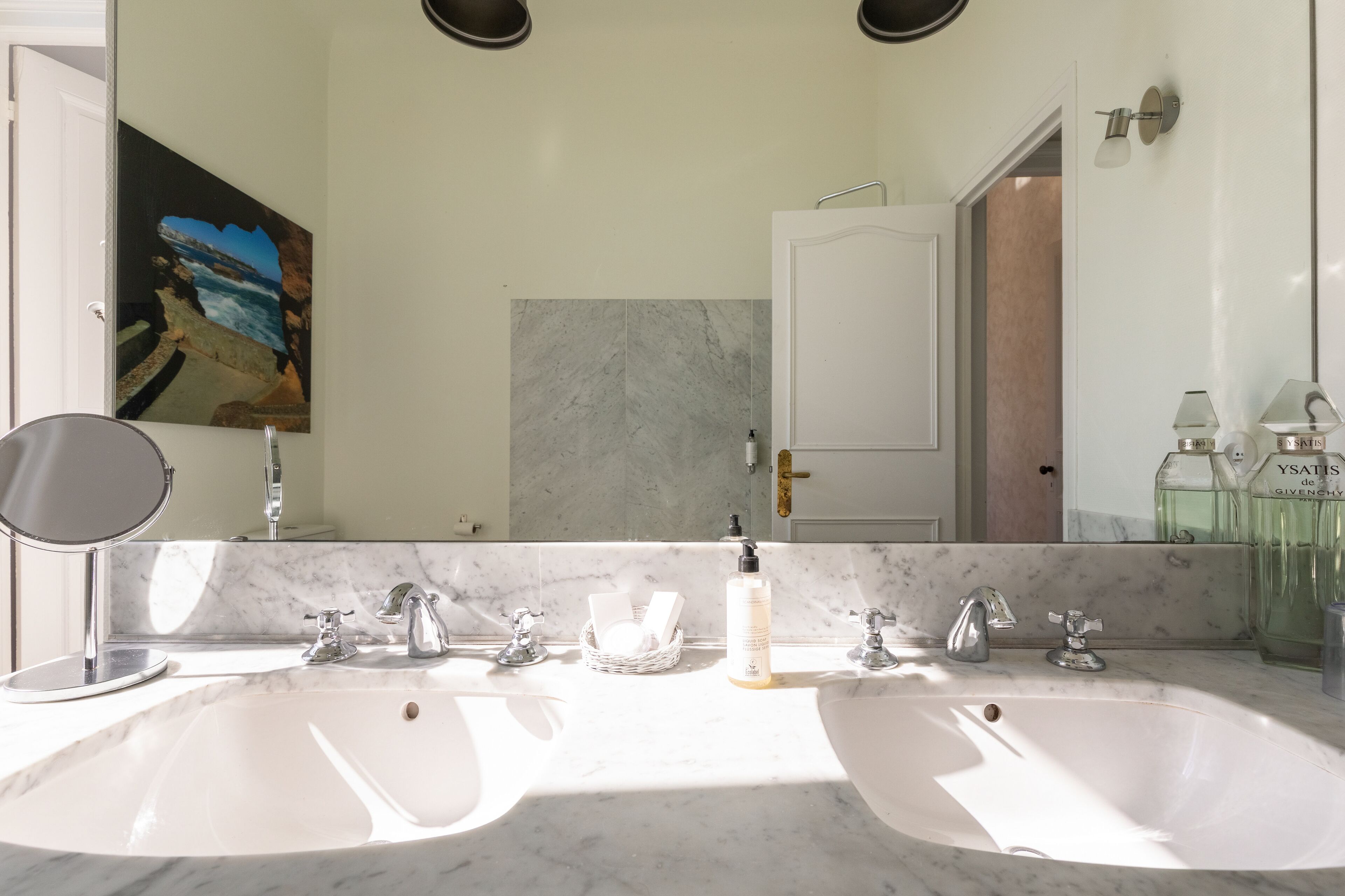 A bathroom with two sinks, a large mirror, and a painting on the wall.