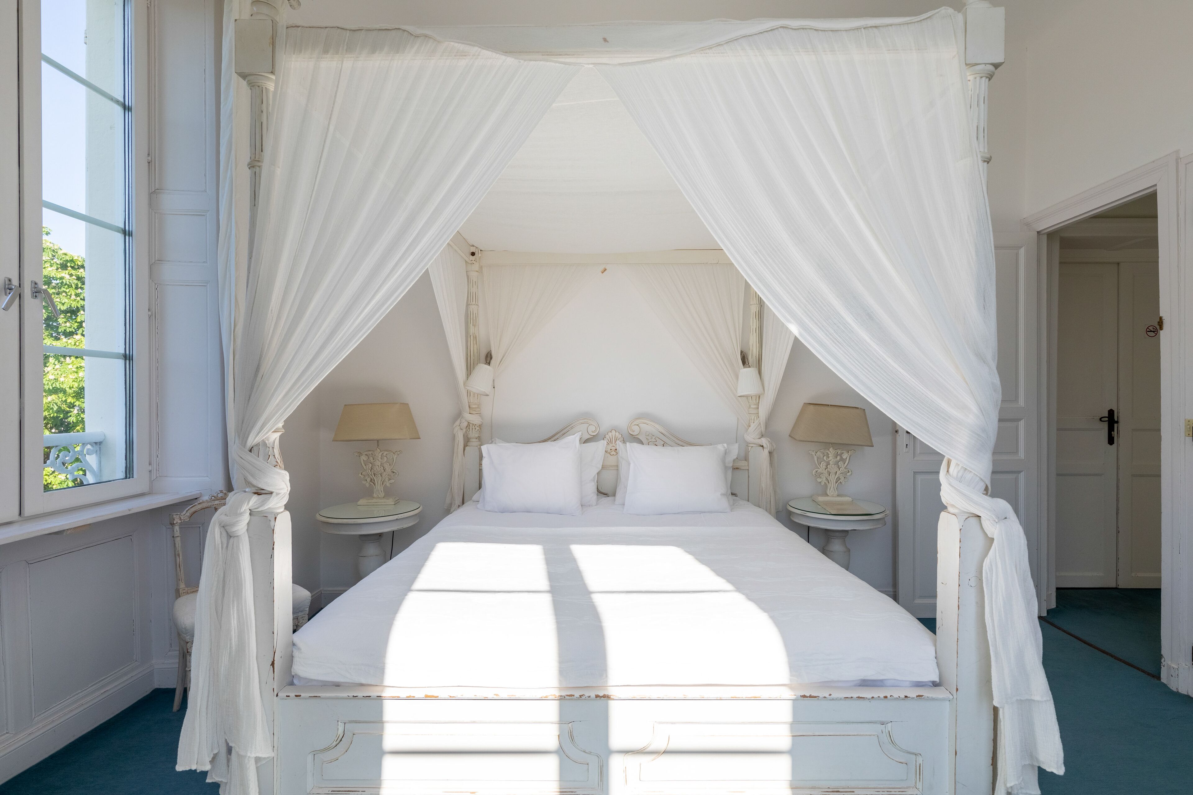 Una cama con dosel y cuatro columnas, con ropa de cama blanca y dos mesitas de noche con lámparas.