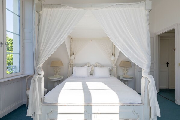 Una cama con dosel y cuatro columnas, con ropa de cama blanca y dos mesitas de noche con lámparas.