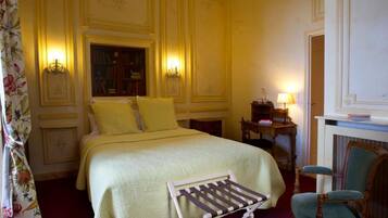 Una habitación de hotel con una cama, una silla, una estantería y una lámpara.