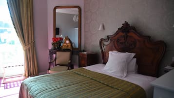 A hotel room with a large bed, a wooden headboard, a mirror, a desk with a chair, and a view of the outdoors.