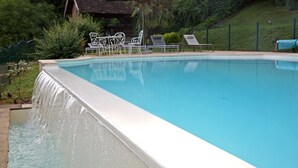 A swimming pool with a waterfall feature, surrounded by lounge chairs and a covered seating area.