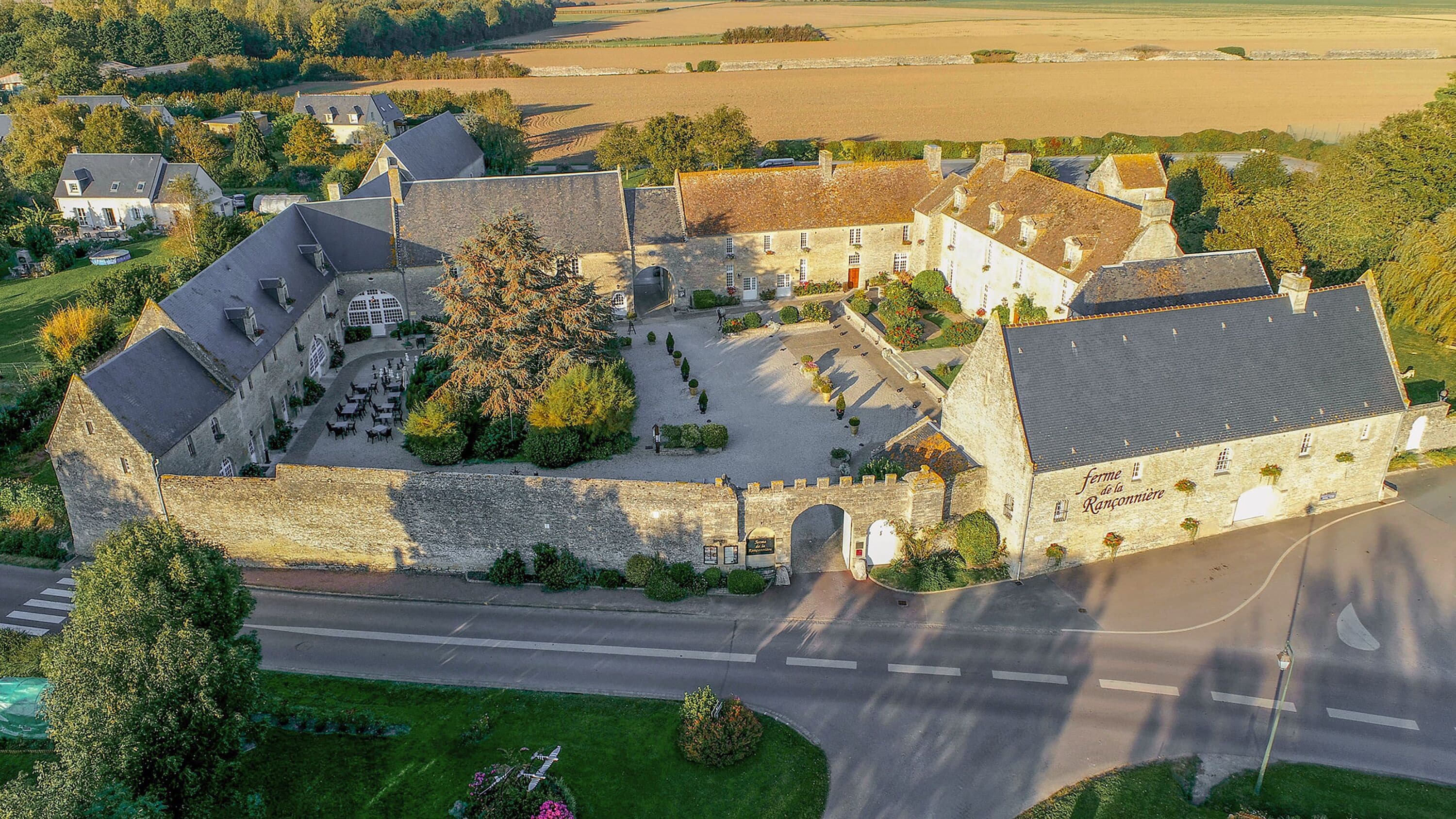 An aerial view of a historic stone building with a courtyard, surrounded by trees and fields.